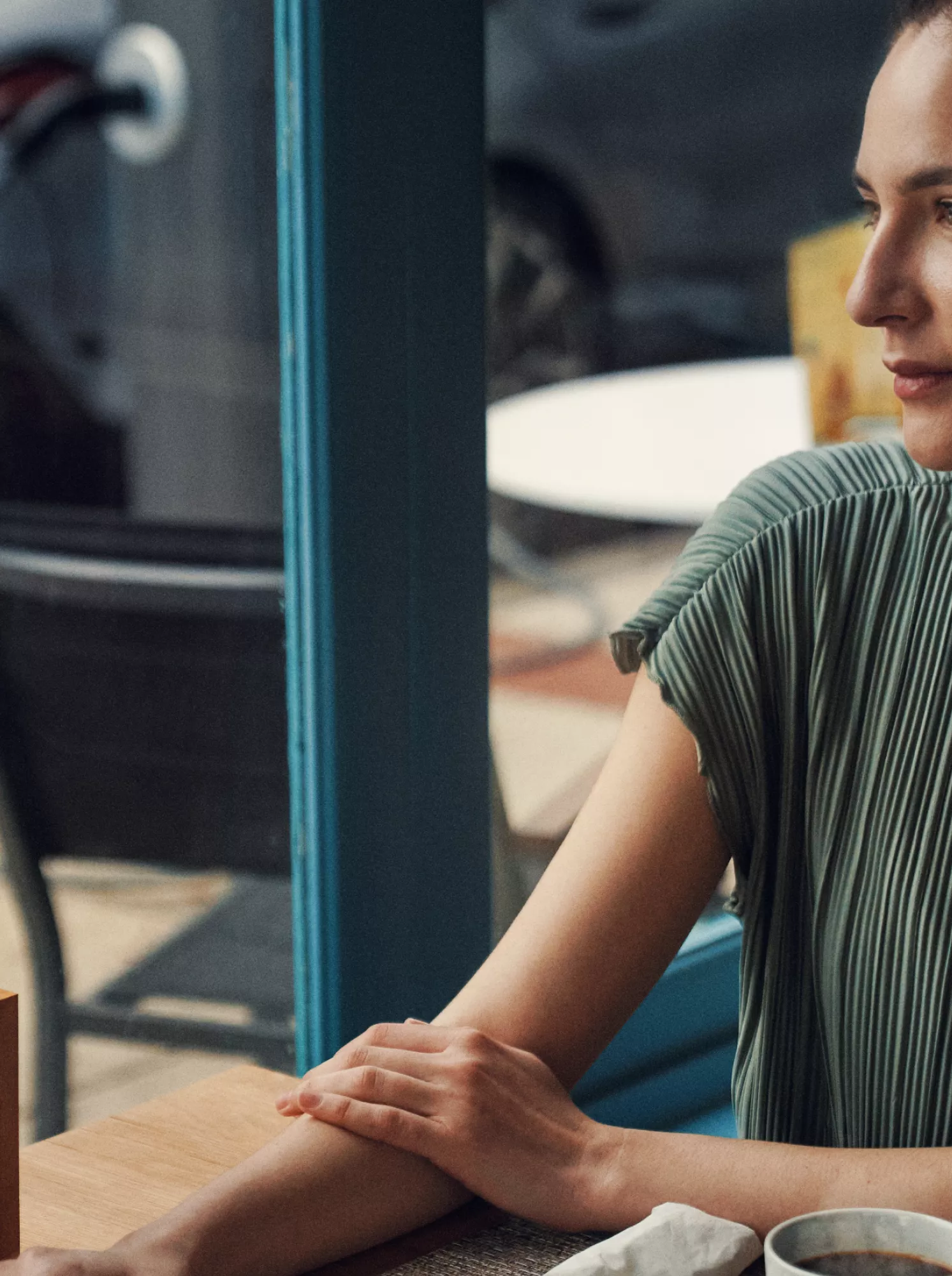 Eine Frau entspannt in einem Café, während ein BMW i5 Touring im Hintergrund geladen wird