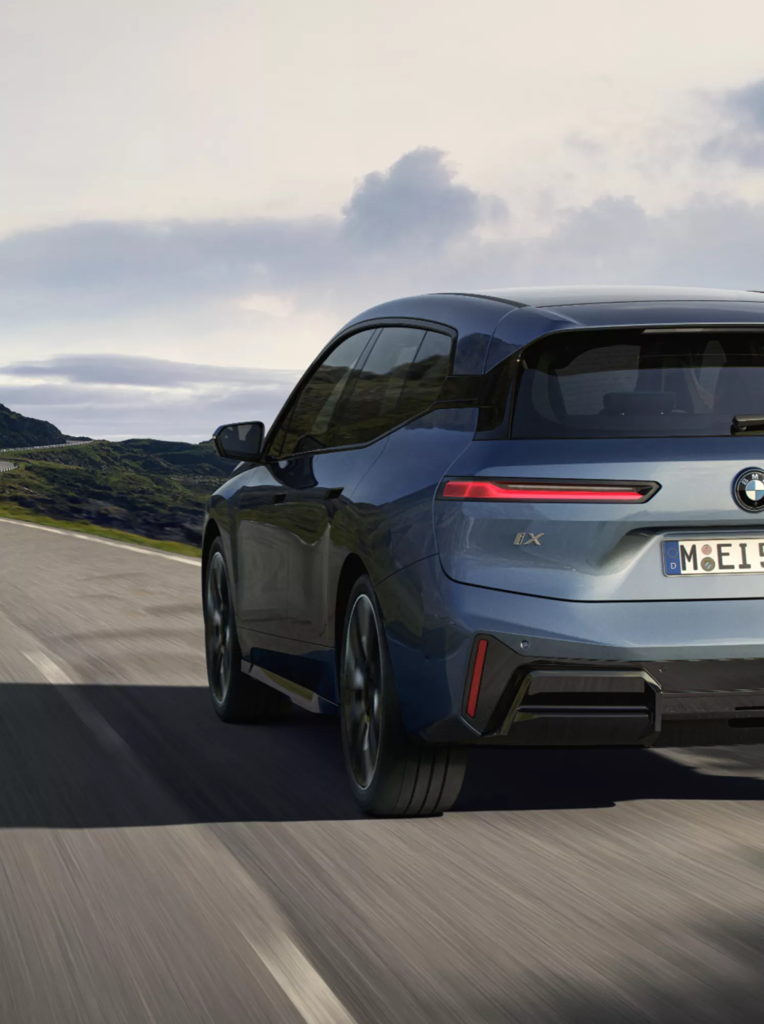 BMW iX fährt auf einer ländlichen Küstenstraße an einem Berghang entlang