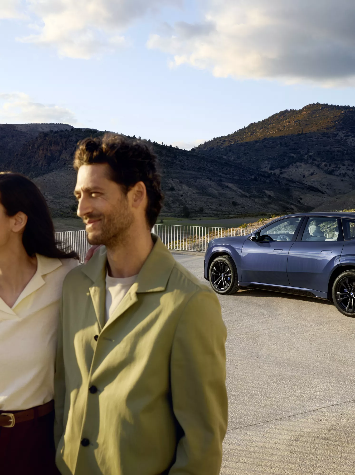 A young couple is standing by a fence, and in the background is a parked BMW iX3
