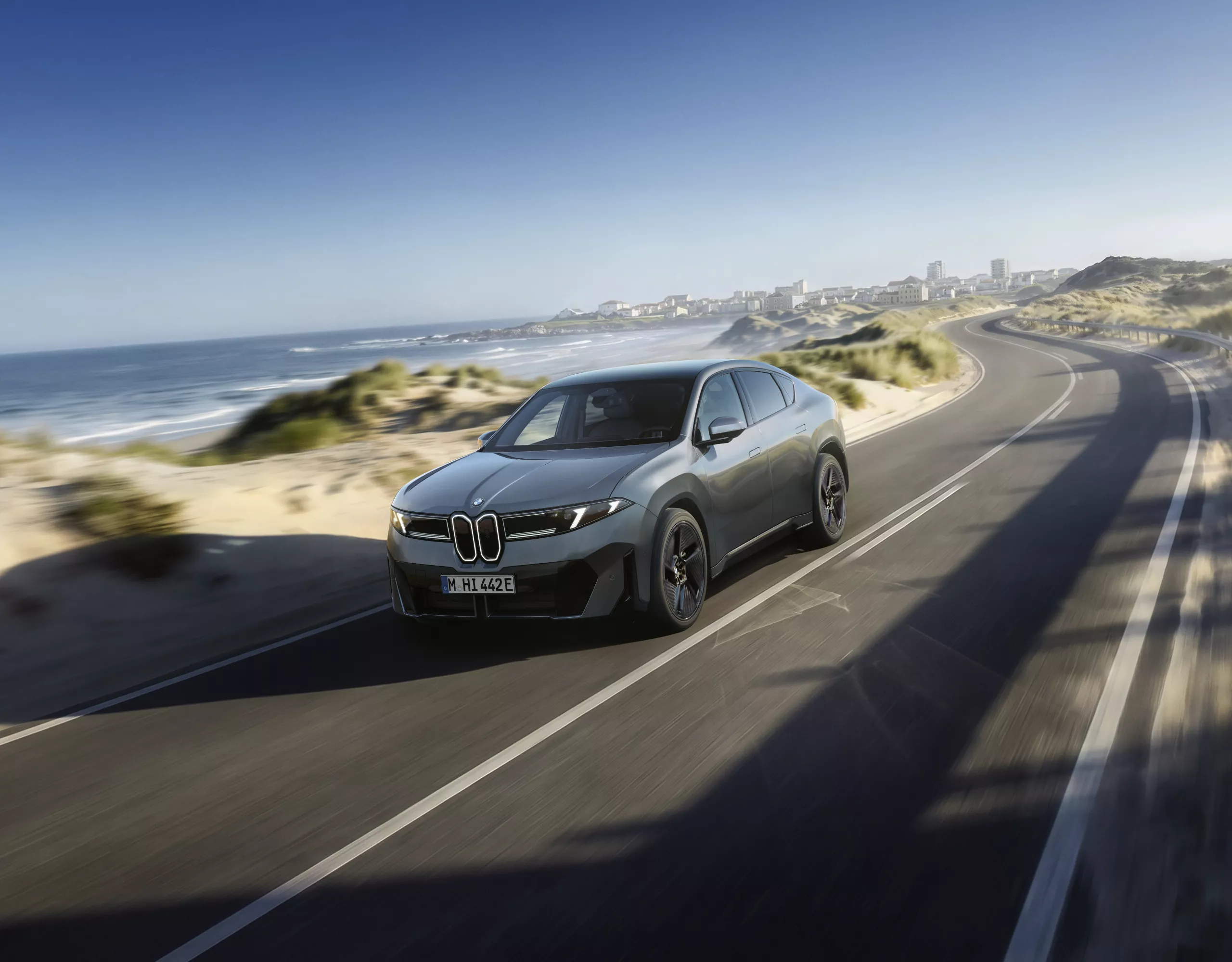 BMW iX4 jede po pobřežní silnici.