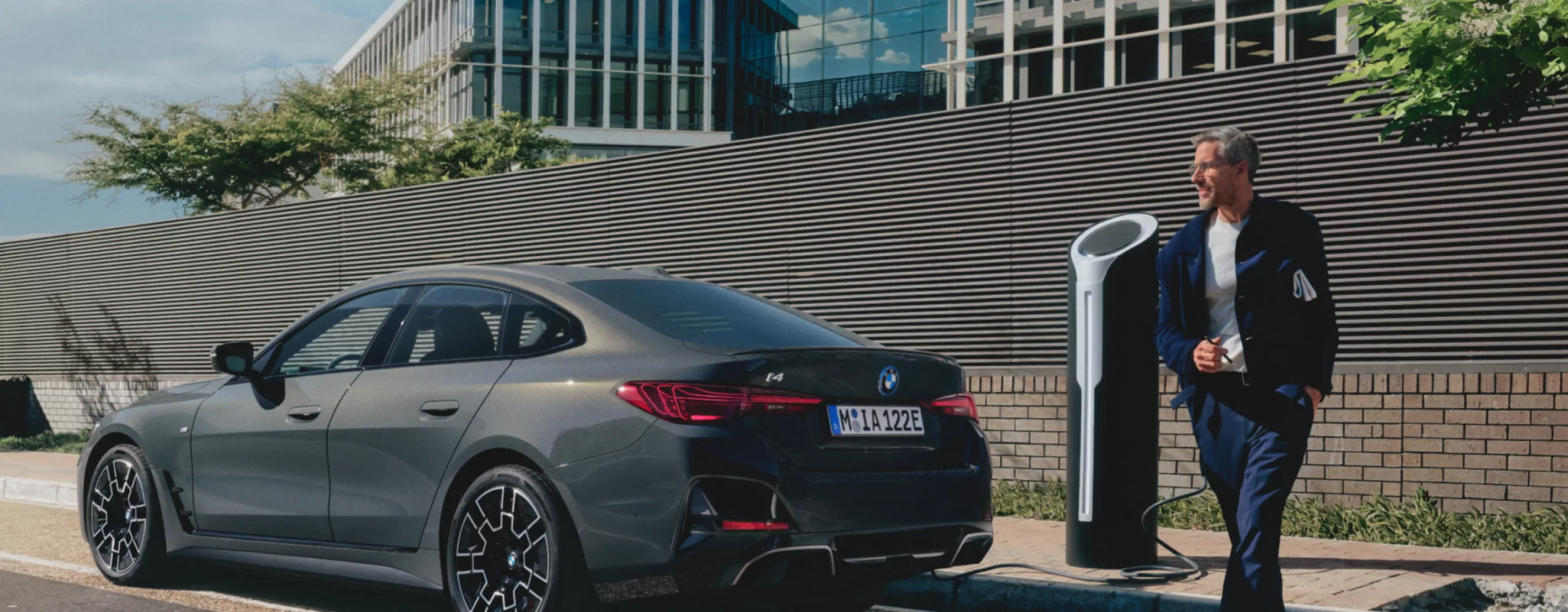 道路の脇で充電中のBMWの背後で立っている人