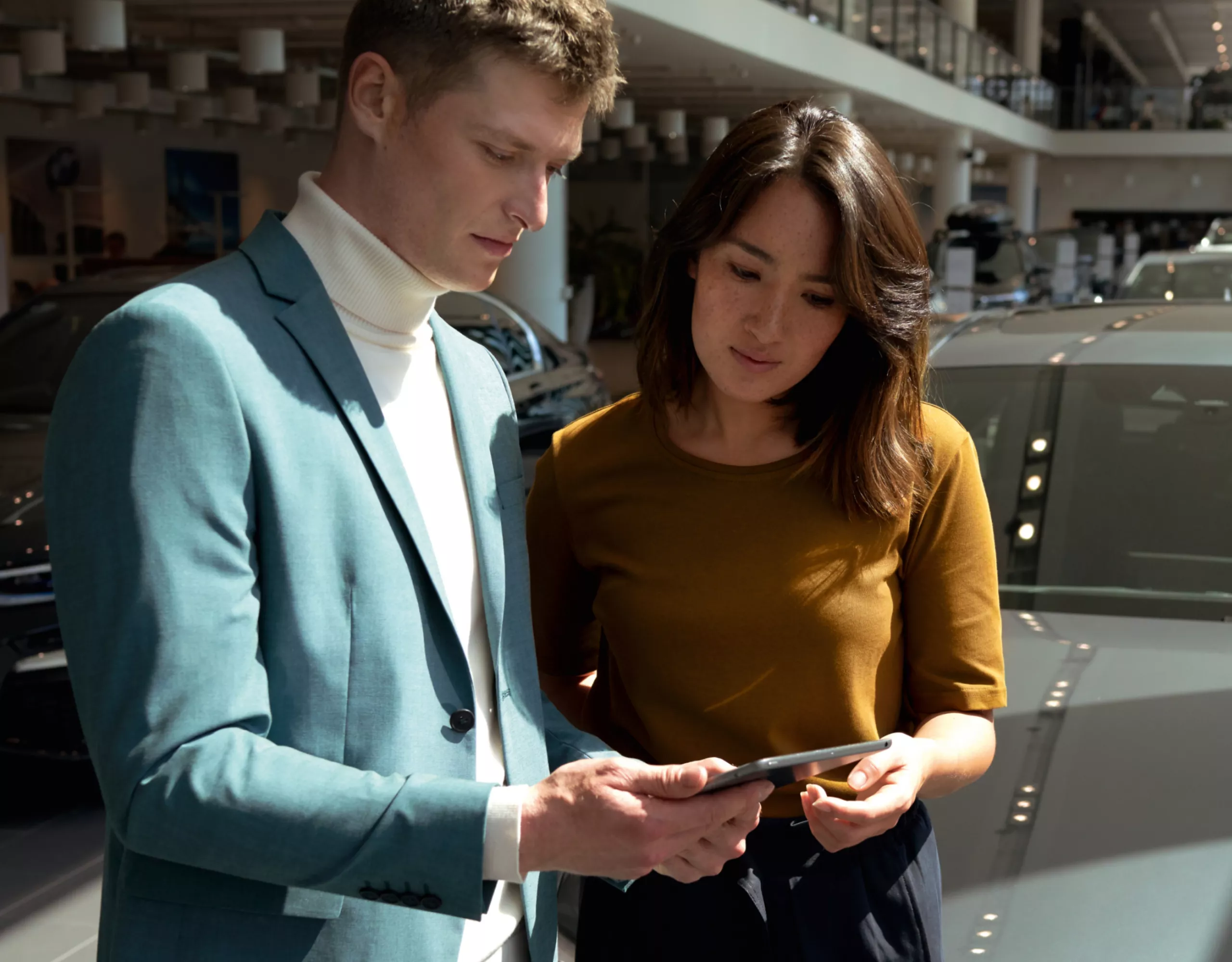 Deux personnes regardent ensemble un appareil mobile chez un concessionnaire automobile