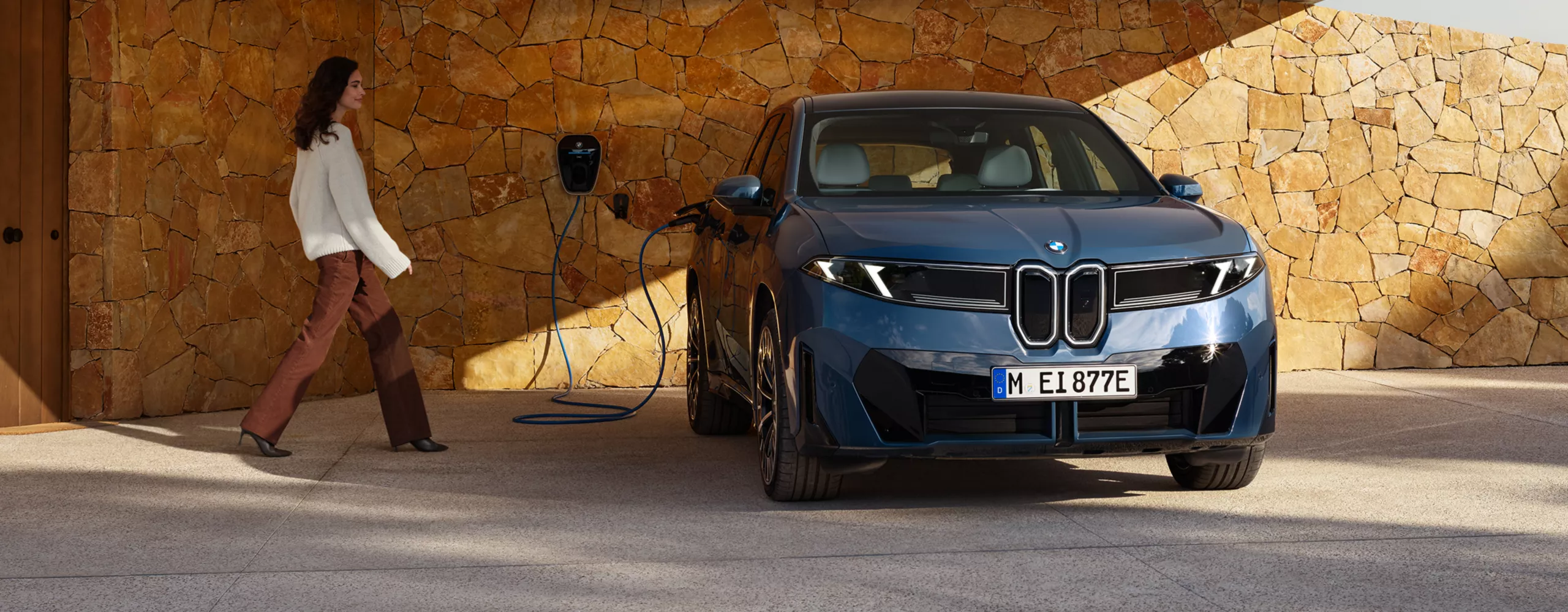 A woman is walking towards a BMW iX3 connected to a wallbox
