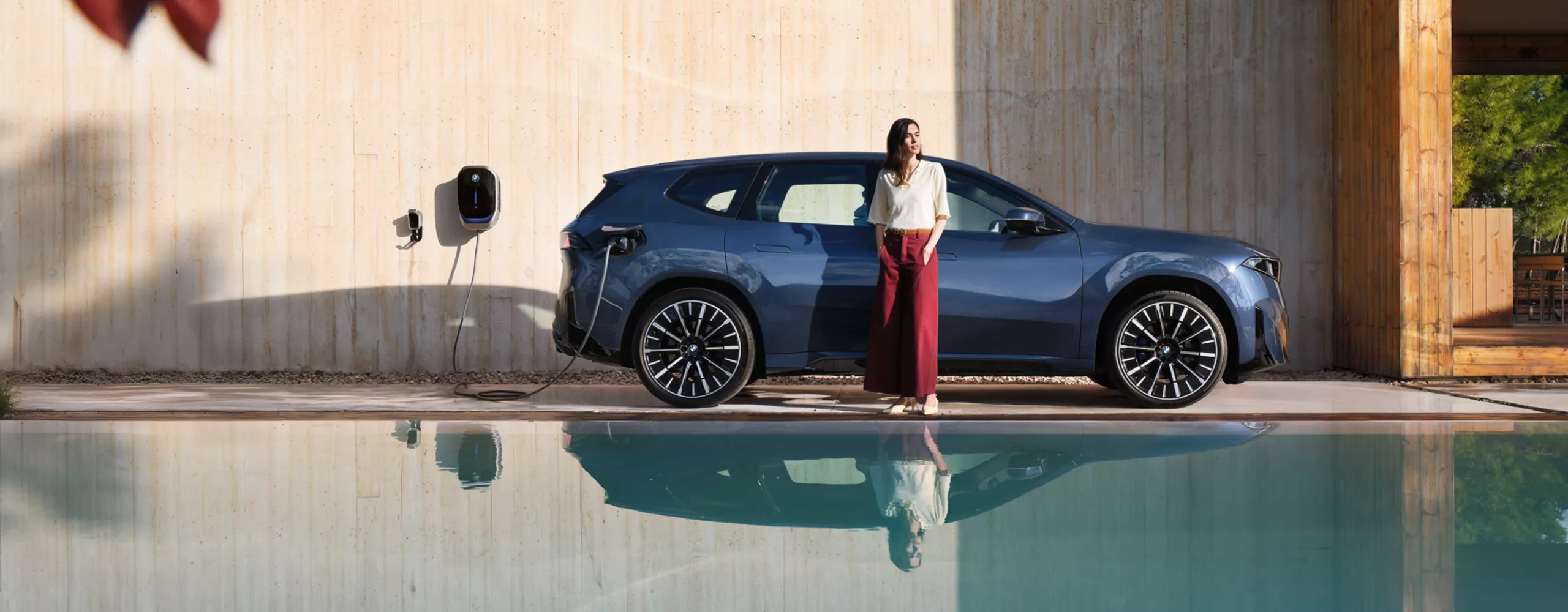 Egy nő egy Wallboxhoz csatlakoztatott BMW iX3 előtt áll