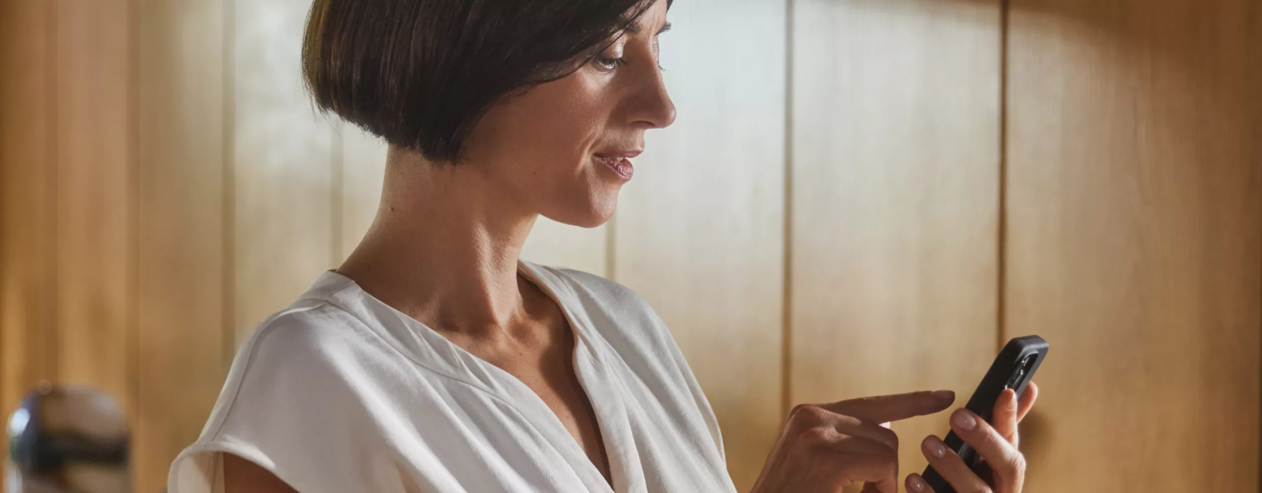 A woman is looking at her smartphone, a wallbox is visible in the background