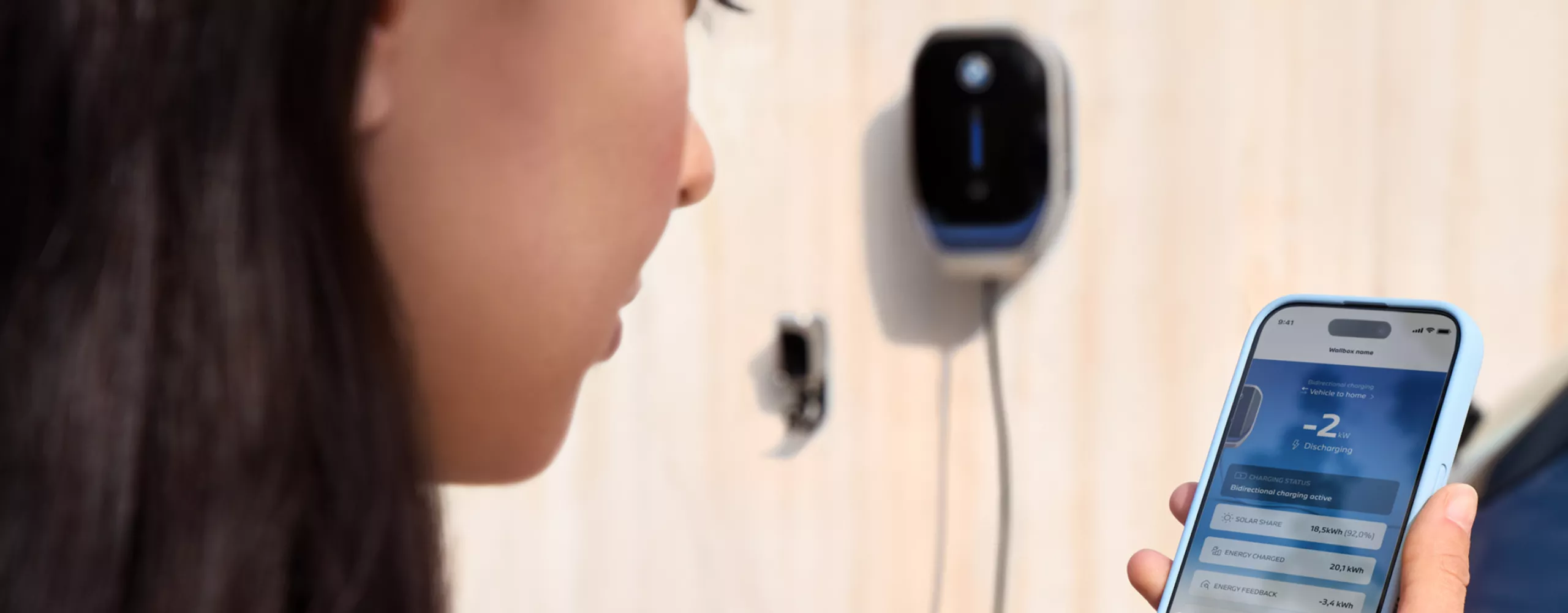A woman is looking at her smartphone, a wallbox is visible in the background
