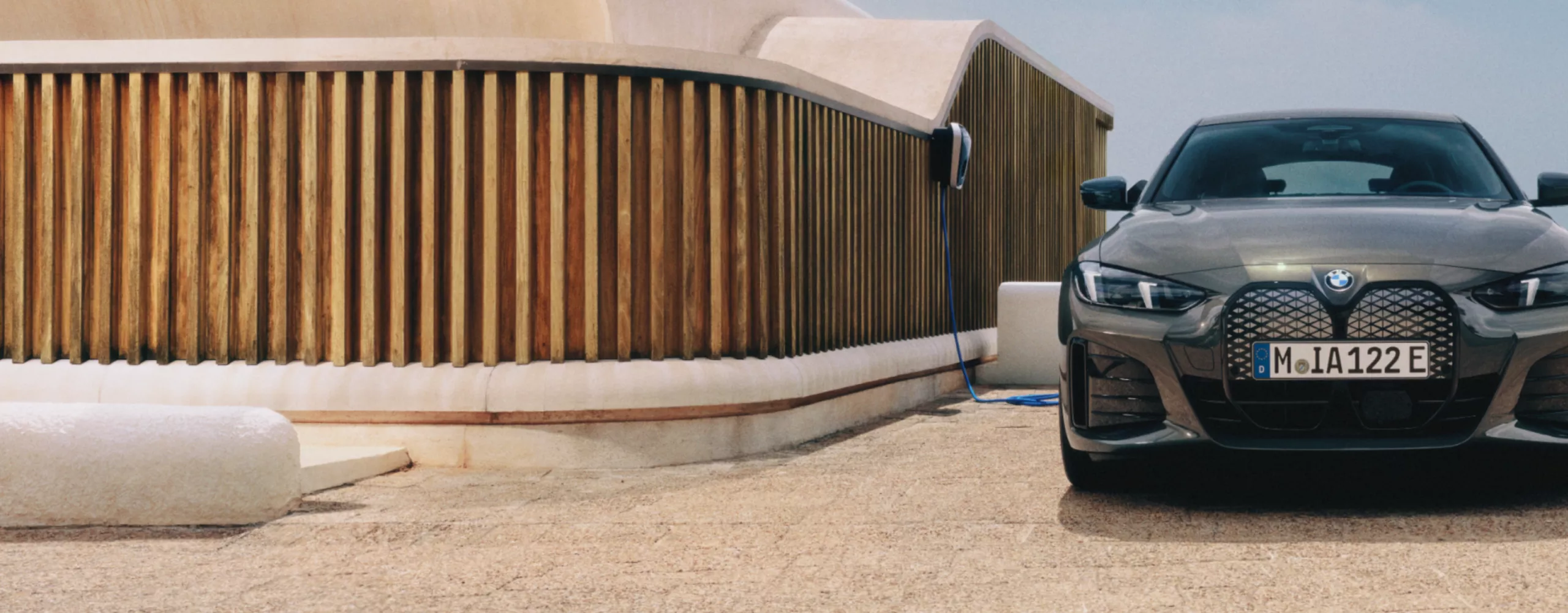 A man with a smartphone is standing next to a BMW i4, which is connected to a wallbox