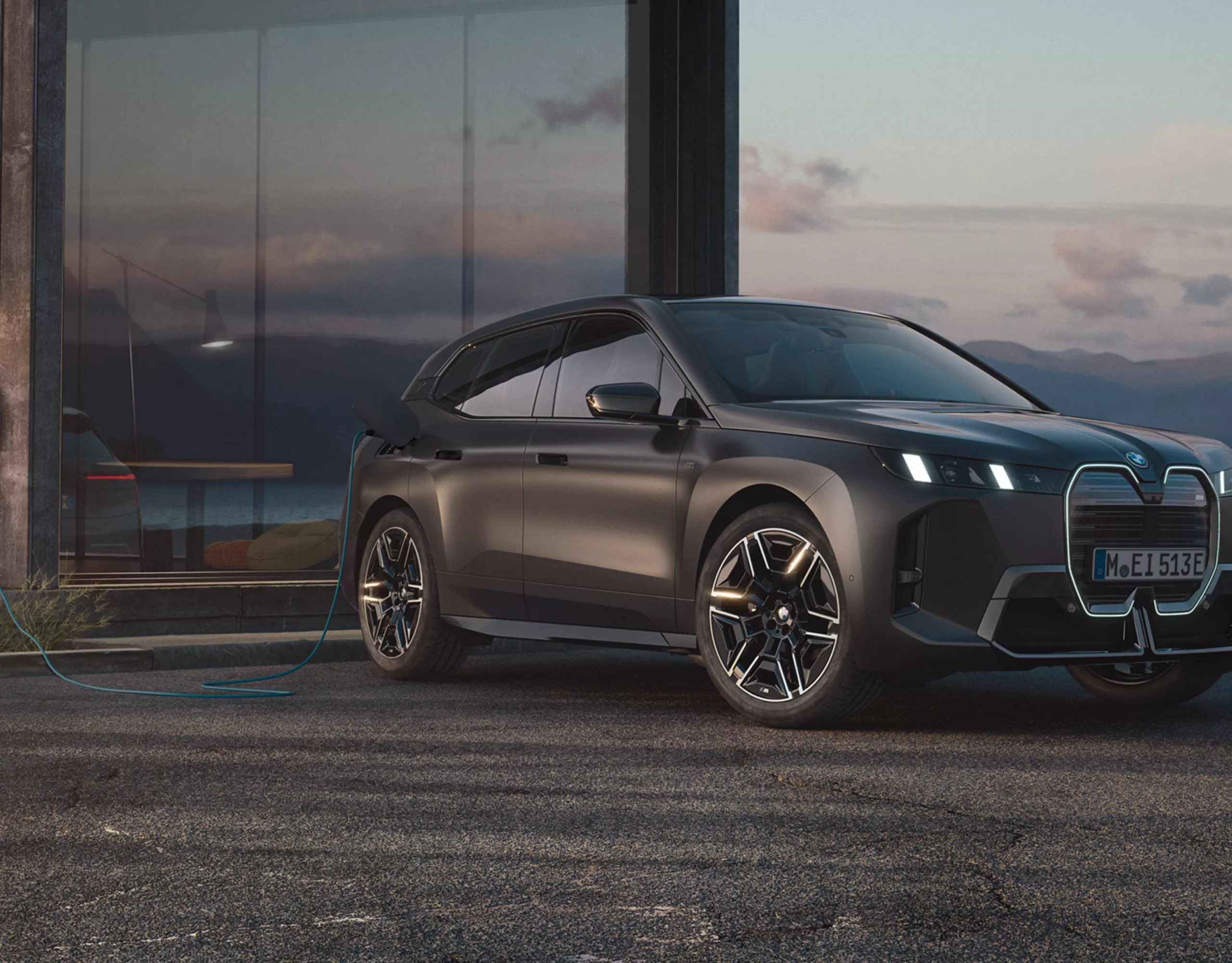Ein BMW iX ist an einer Wallbox vor einem Haus vor einem See angeschlossen