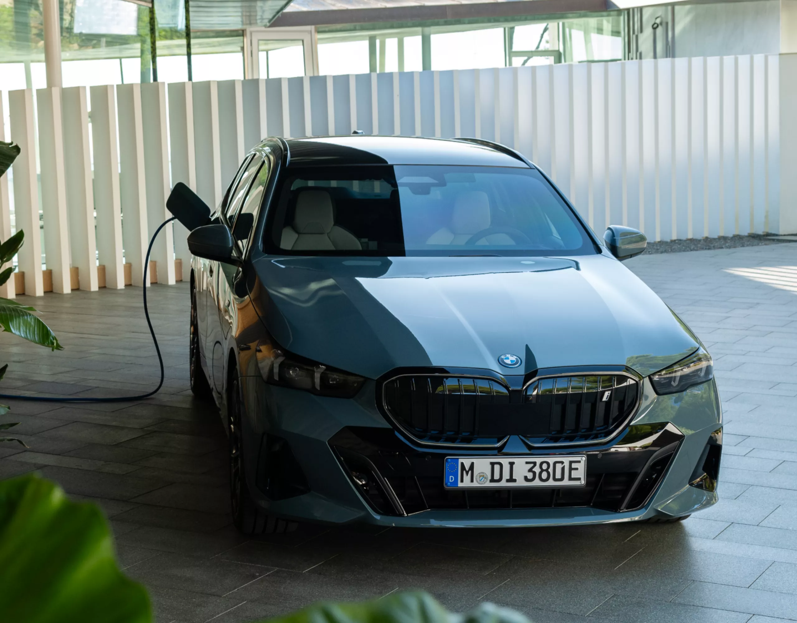 En BMW i5 er parkert på en privat parkeringsplass. En ladekabel er koblet til ladeporten