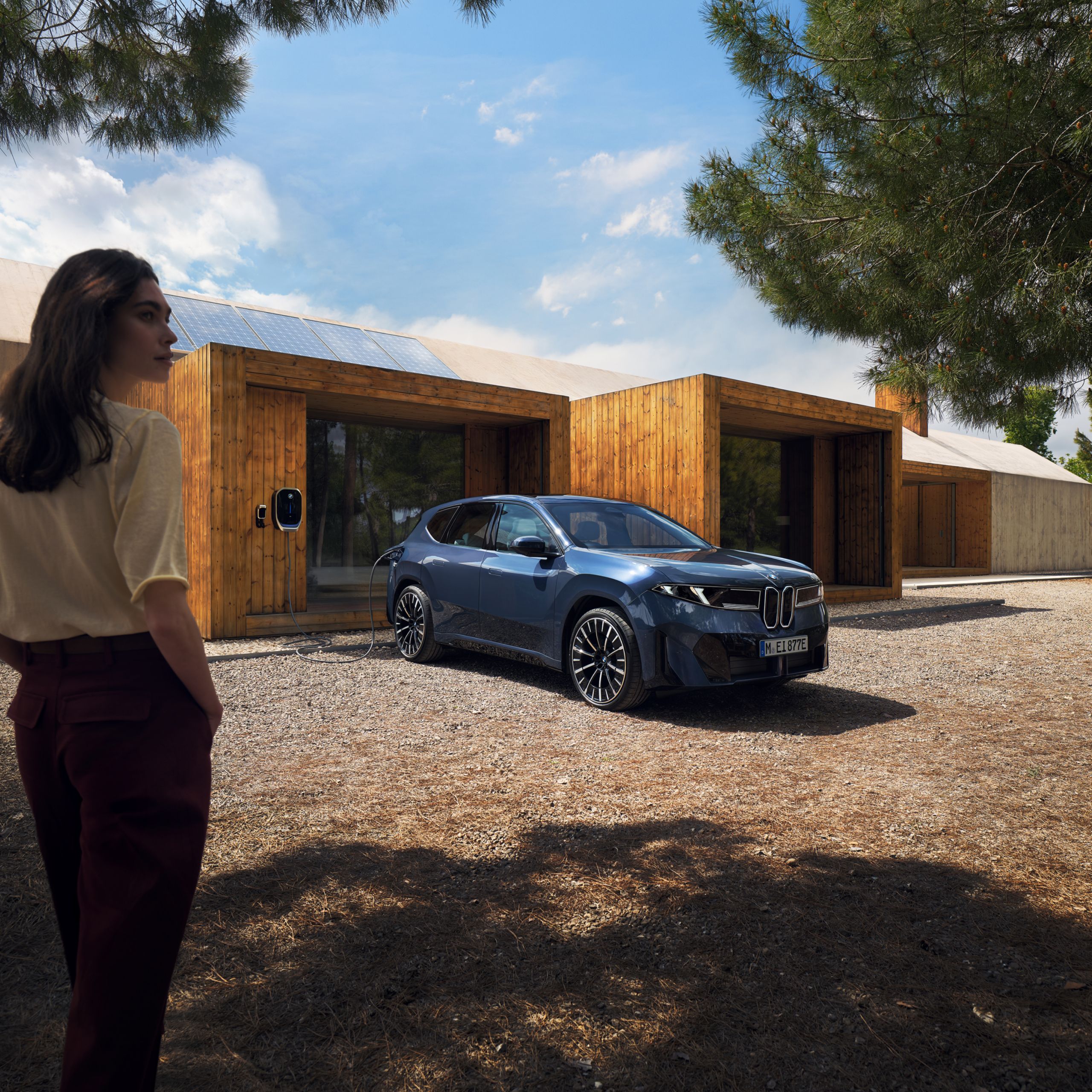 Eine Frau geht auf einen BMW iX3 zu, der an einer Wallbox angeschlossen ist