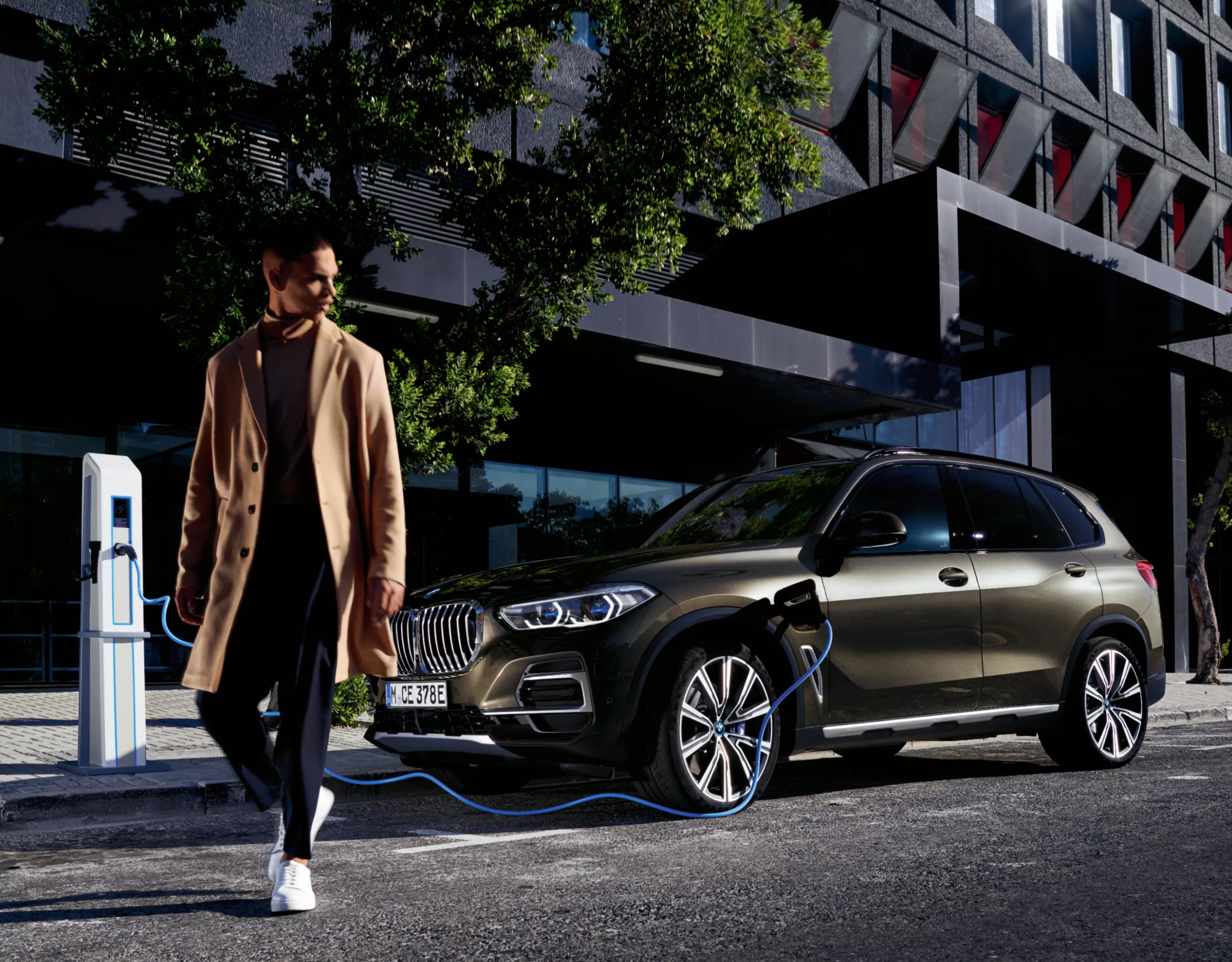 Three persons are standing in front of a BMW along with a car salesman inside a dealership