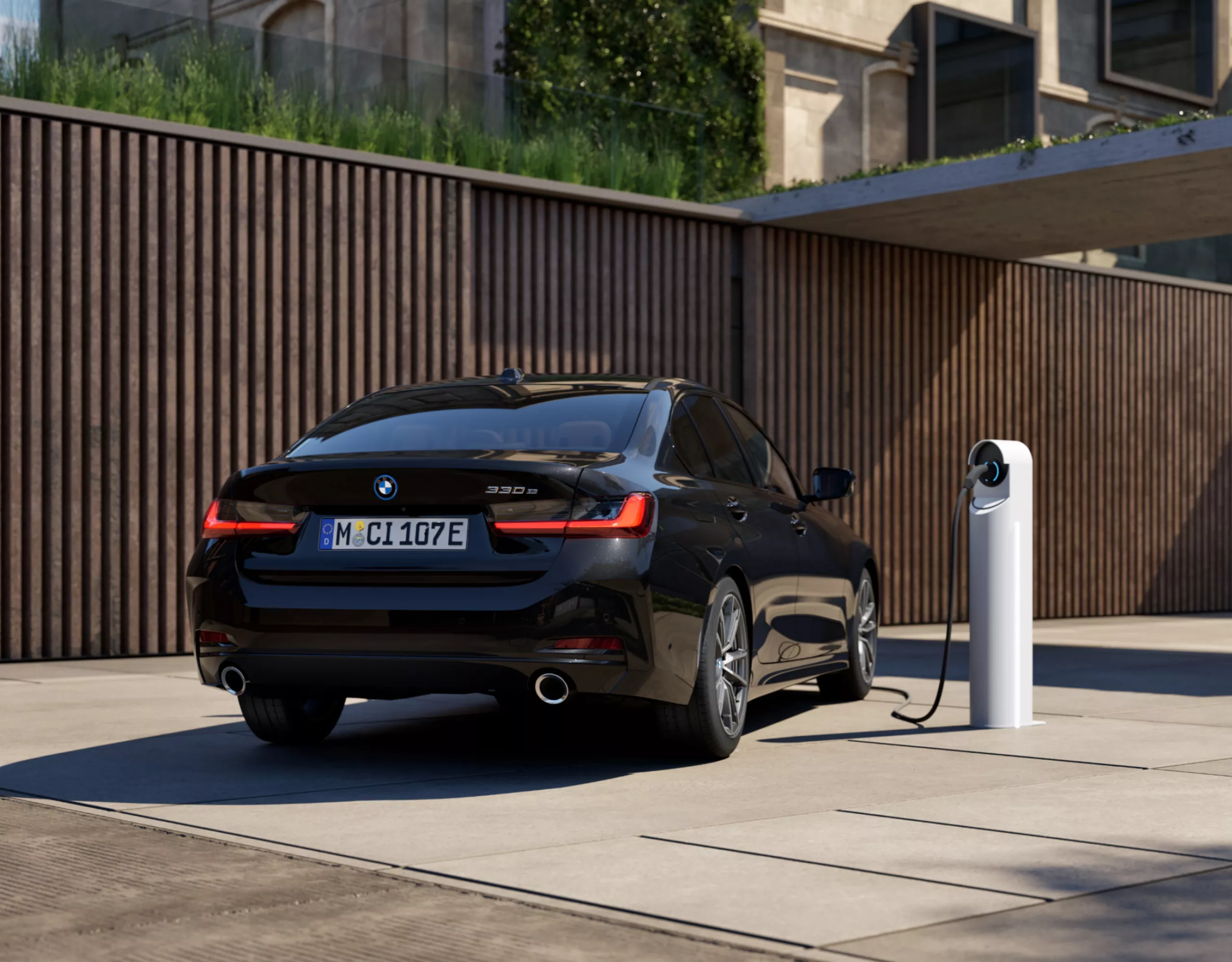 Une BMW Plug-in Hybride est rechargée sur une borne de recharge publique située devant une maison moderne