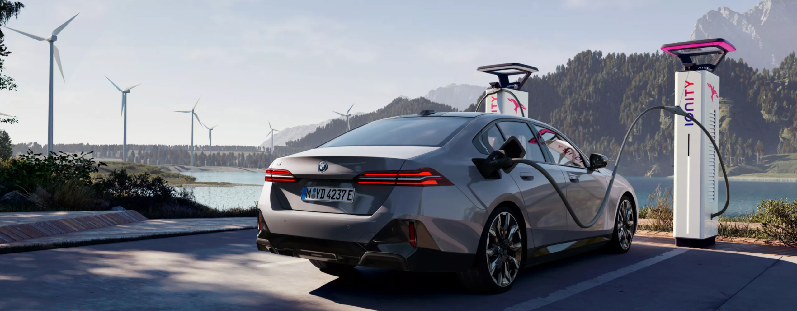 BMW laddar vid en laddstation med utsikt över vatten, berg och vindkraftverk
