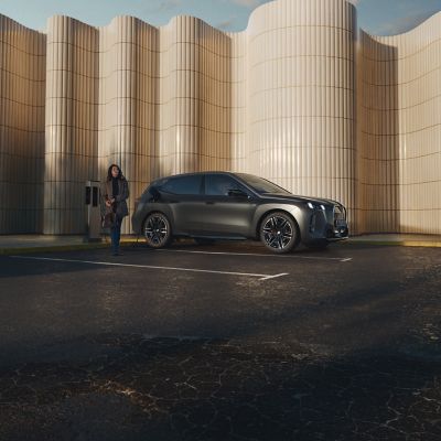 Person leaning against a BMW at a public charging post at the side of the road