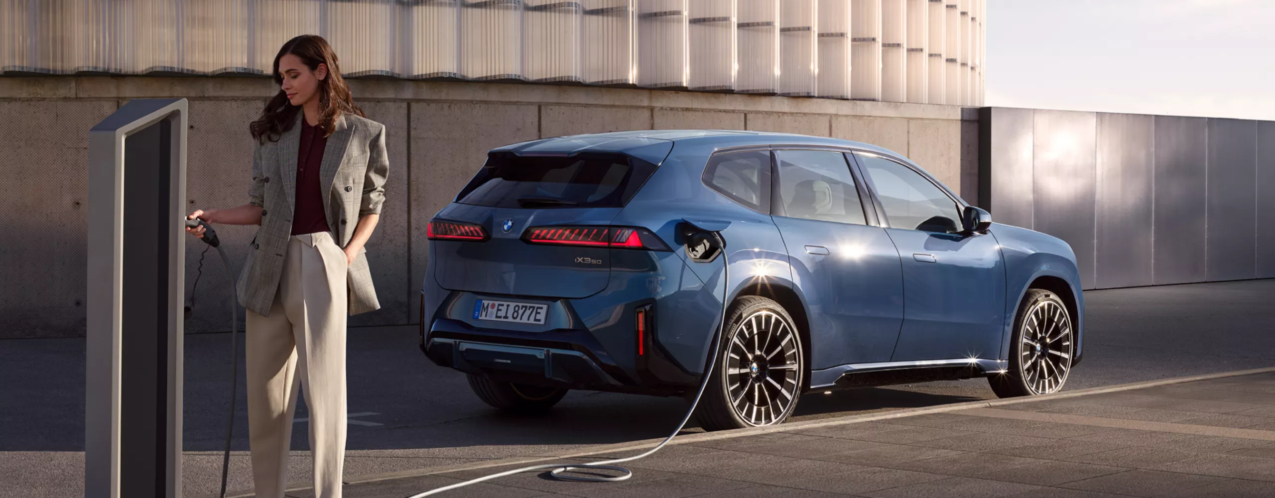 En man står bredvid en BMW iX3, som är ansluten till en publik laddstation