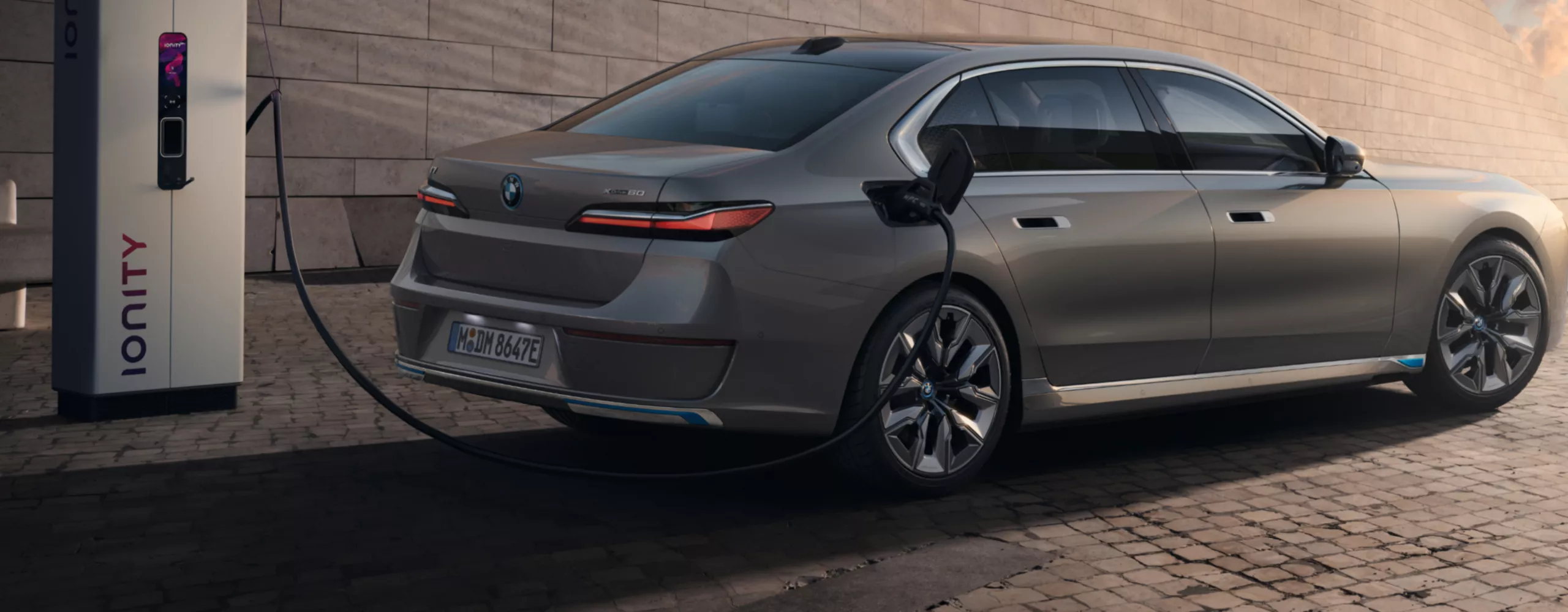 A woman is standing next to a BMW iX3, which is connected to a public charging station