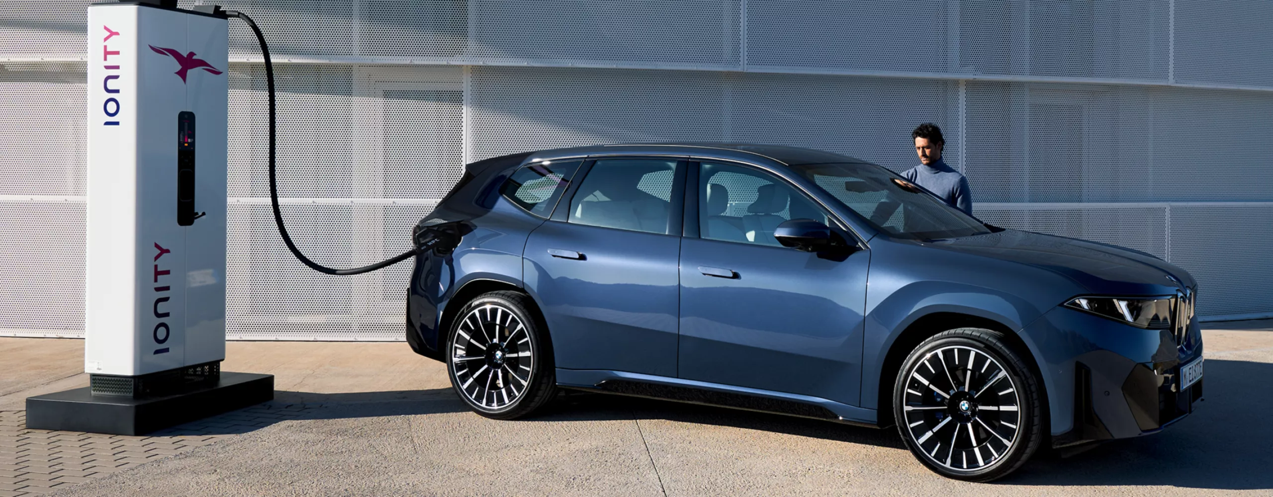 Ein Mann steht neben einem BMW iX3, der an einer öffentlichen Ladesäule angeschlossen ist
