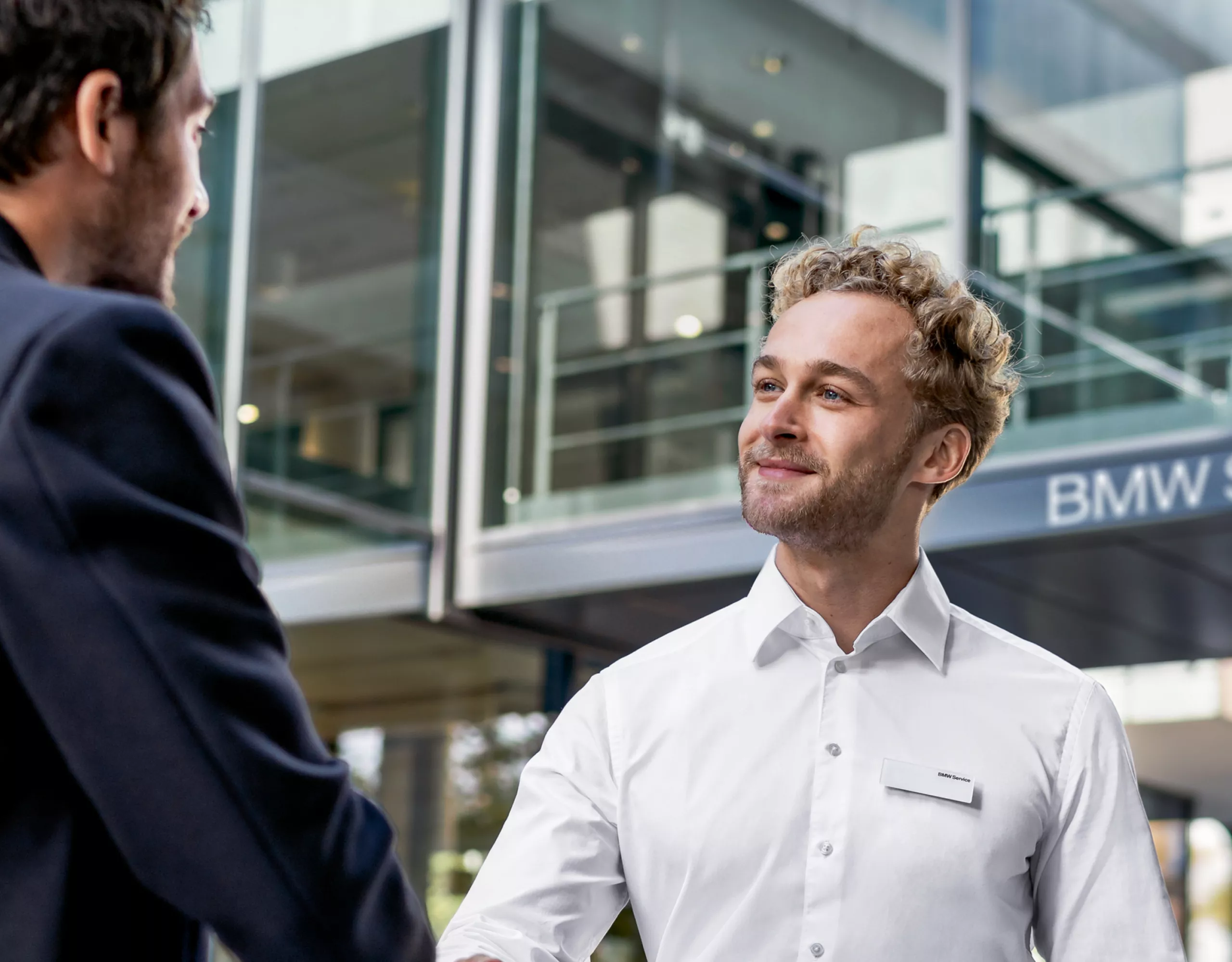 Two men are shaking hands in front of a BMW service area