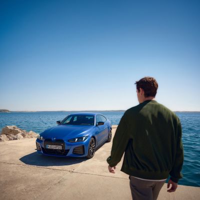 Une personne s'approche d'une BMW garée en bord de mer