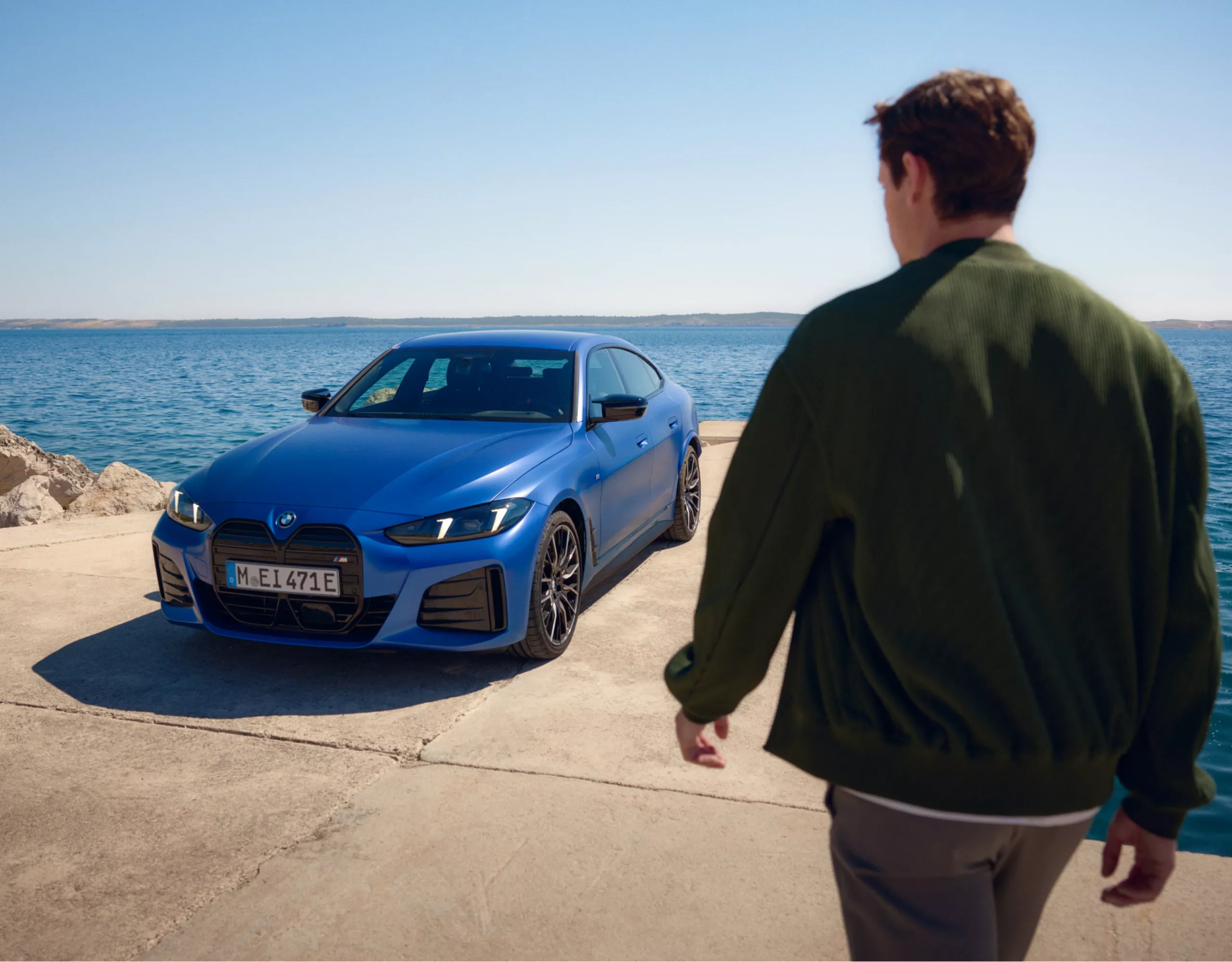 Person walking towards a BMW parked by the sea