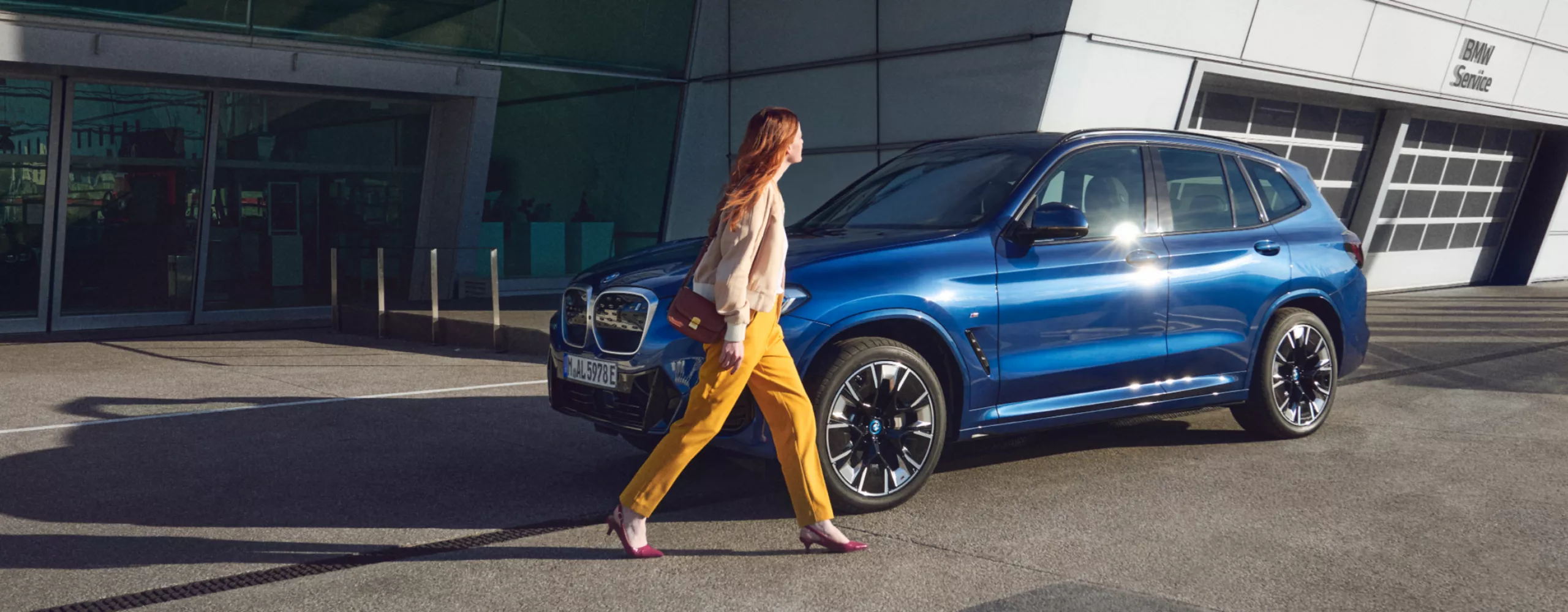 Een vrouw loopt langs een blauwe BMW voor een BMW dealer