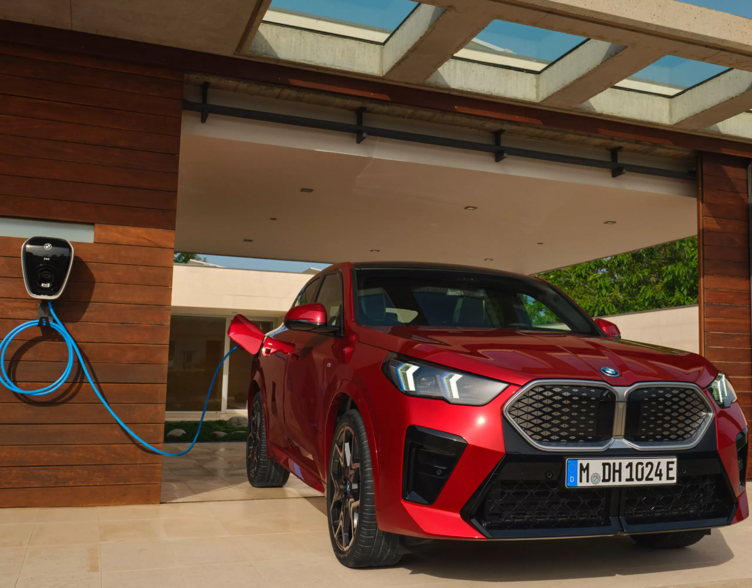 Red BMW iX2 connected to a wallbox in front of a garage