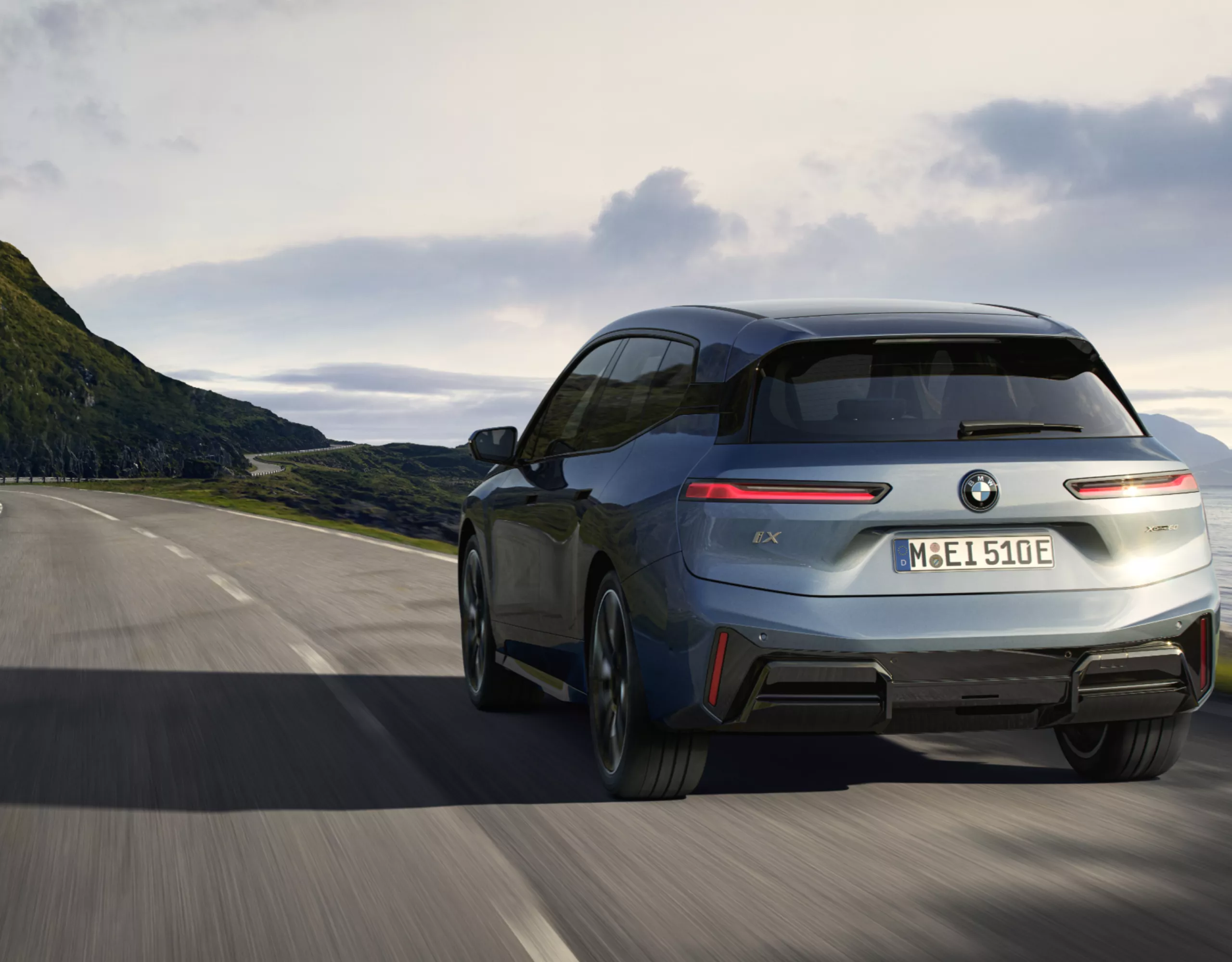 A grey-blue BMW drives along a landscape with hills