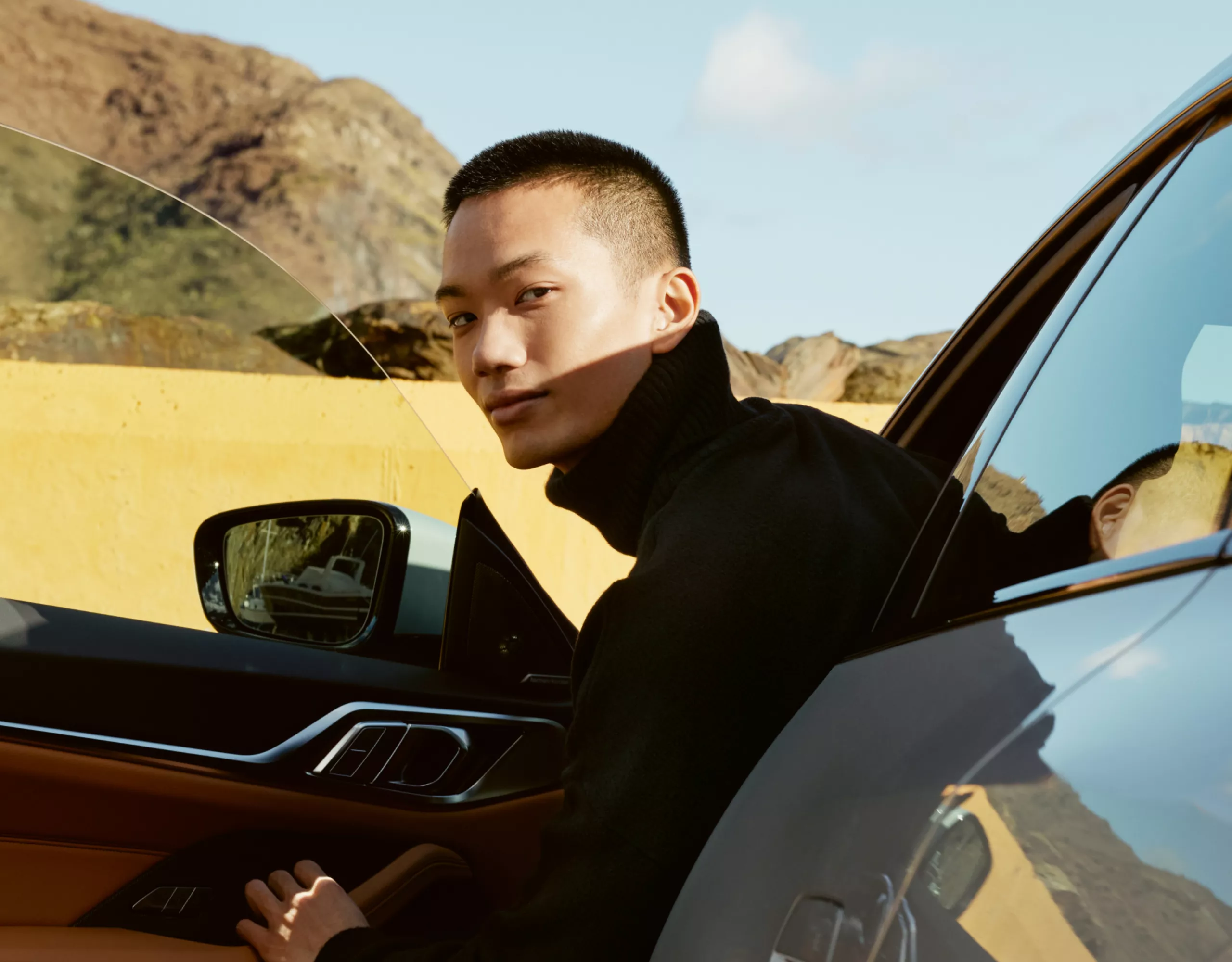 A young man is leaning out of the drivers seat of a parked car with its door opened