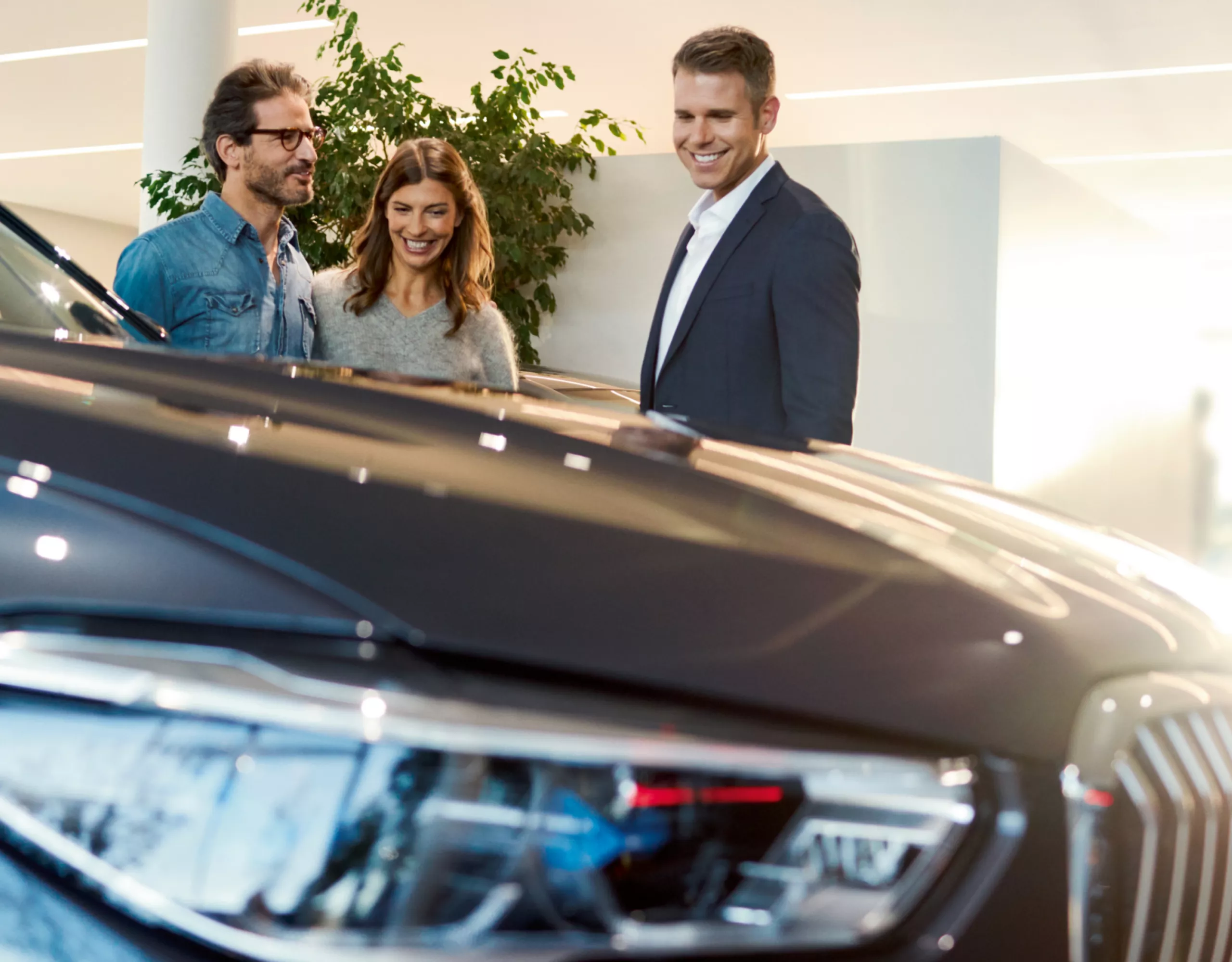 Drei Personen stehen mit einem Autoverkäufer vor einem BMW im Autohaus