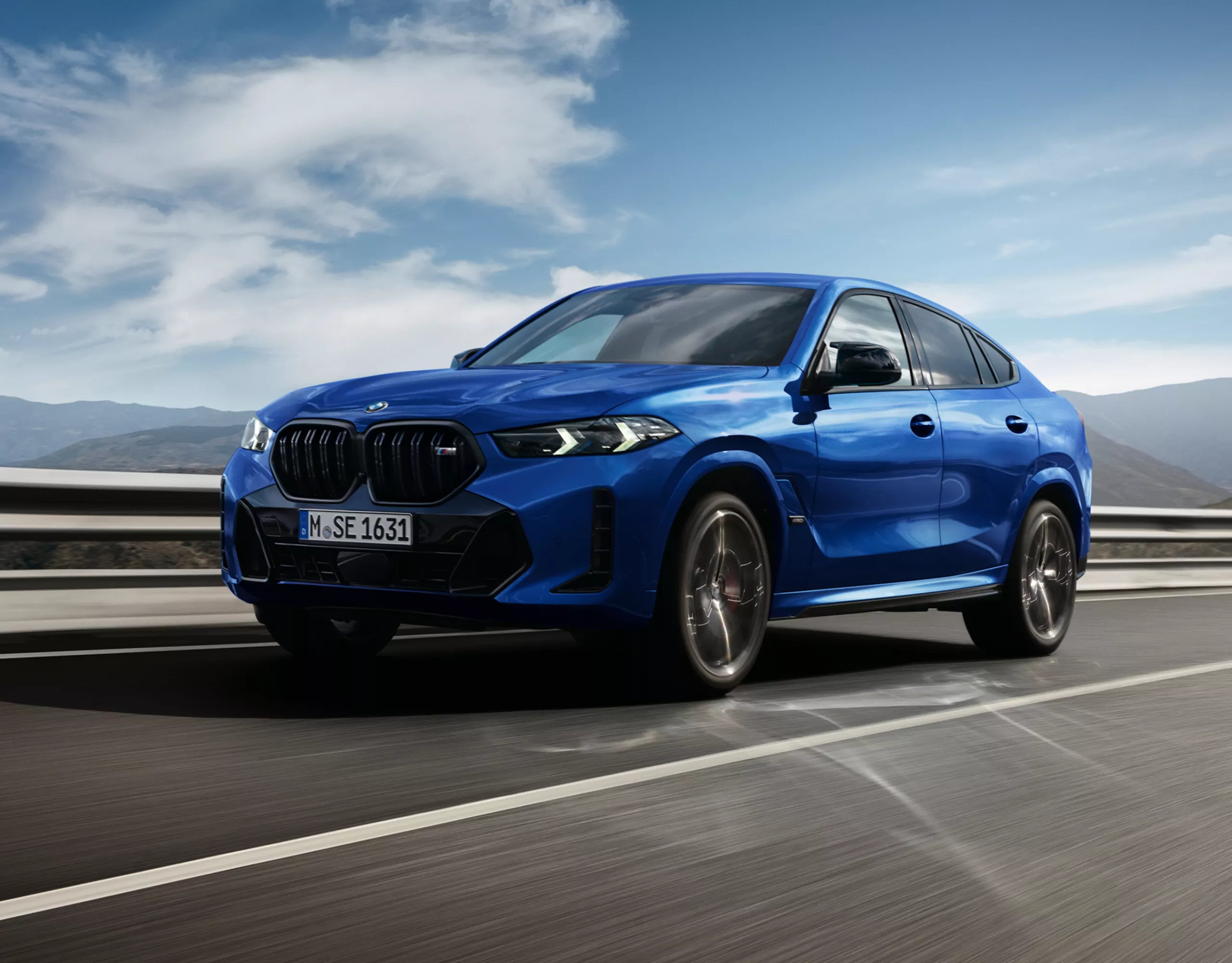 Ein BMW X6 M60i xDrive fährt mit hoher Geschwindigkeit über die Autobahn vor einem Bergpanorama
