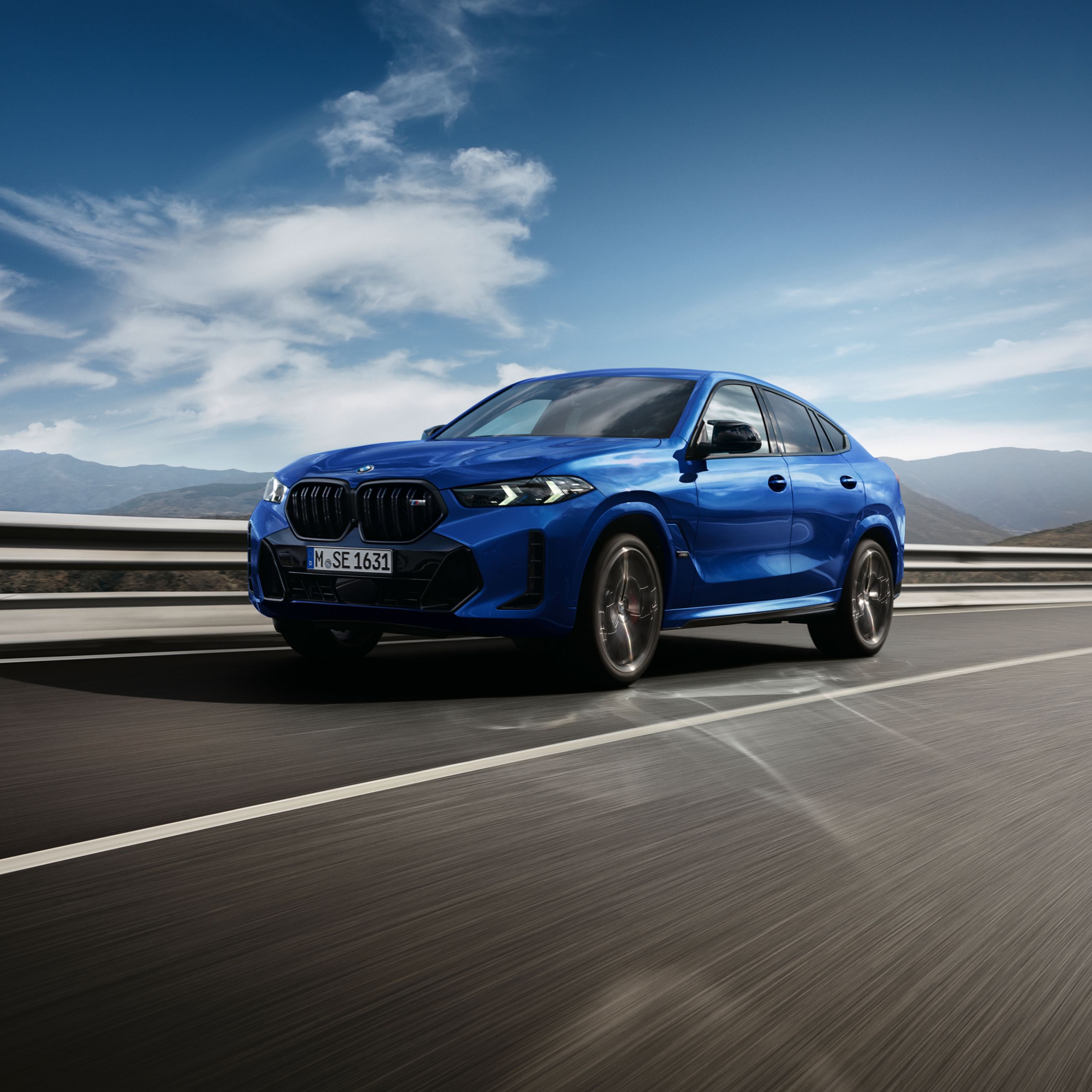 Voor een berglandschap rijdt een BMW X6 M60i xDrive met hoge snelheid over de snelweg
