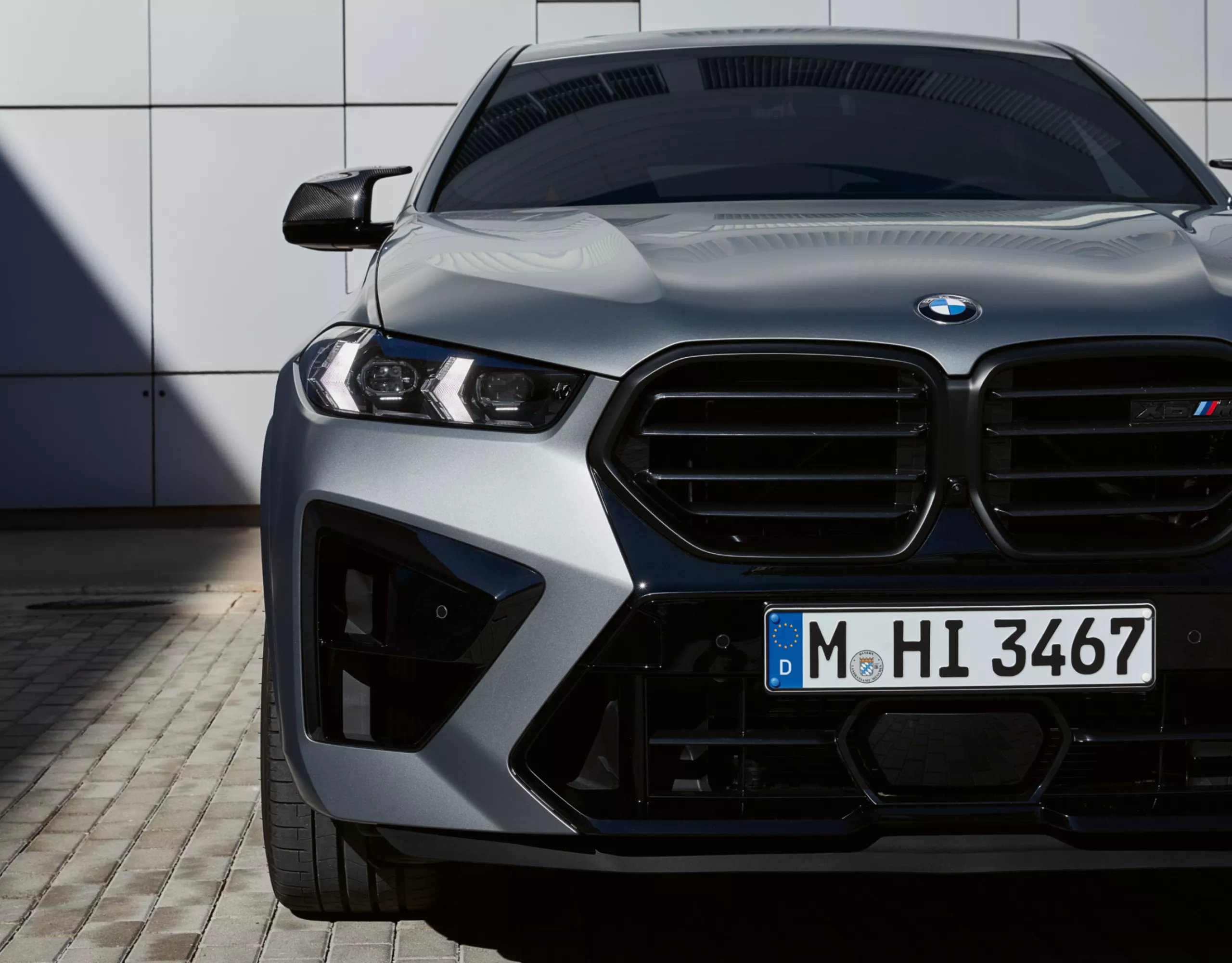 회색 벽 앞에 주차된 BMW X6 M 컴페티션의 전면 모습