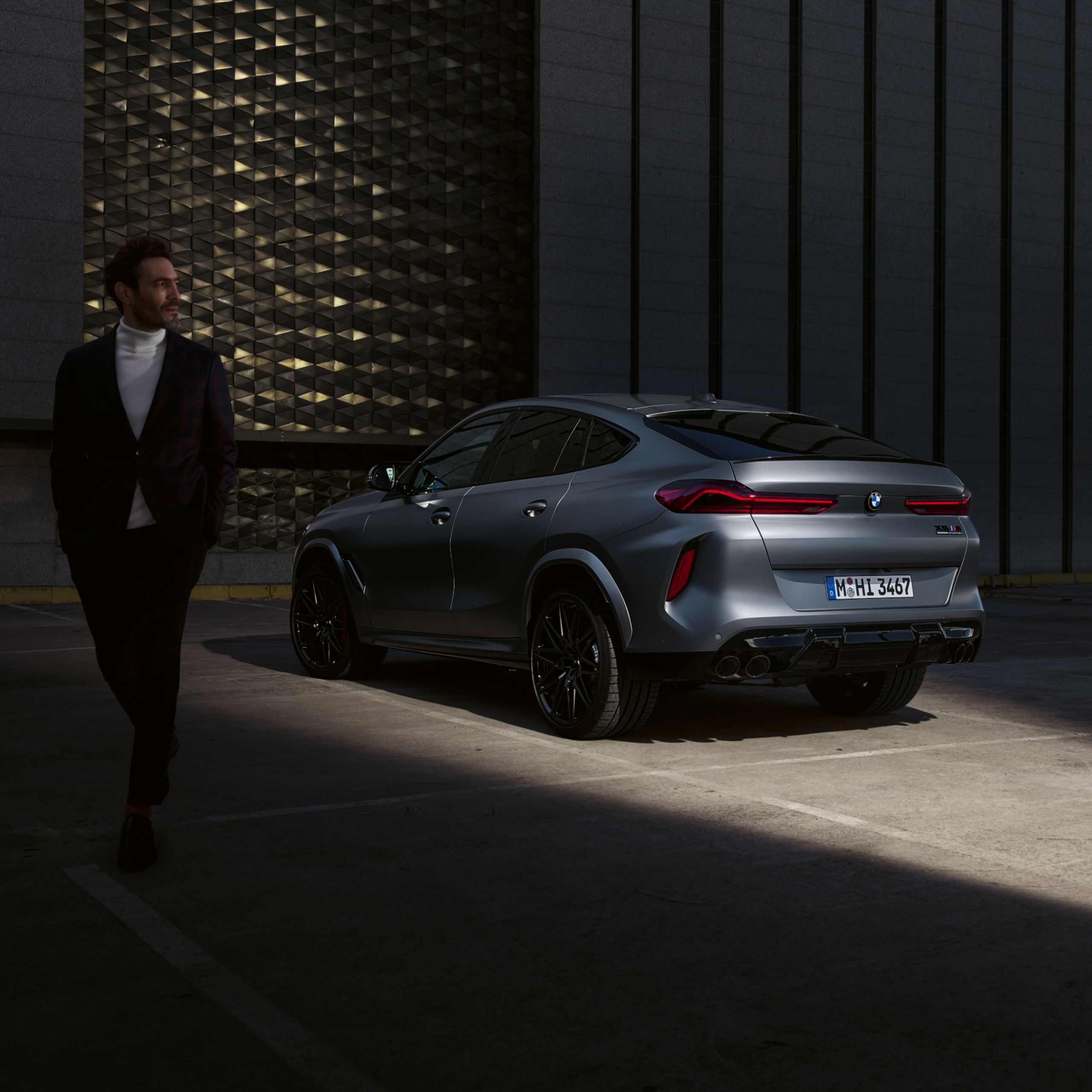 Persoon in de schaduw voor een BMW X6 die in de halfschaduw geparkeerd staat