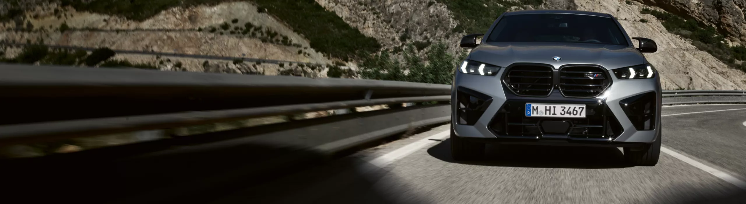 BMW X6 M Competition fährt auf einer kurvigen Landstraße durch ein Tal