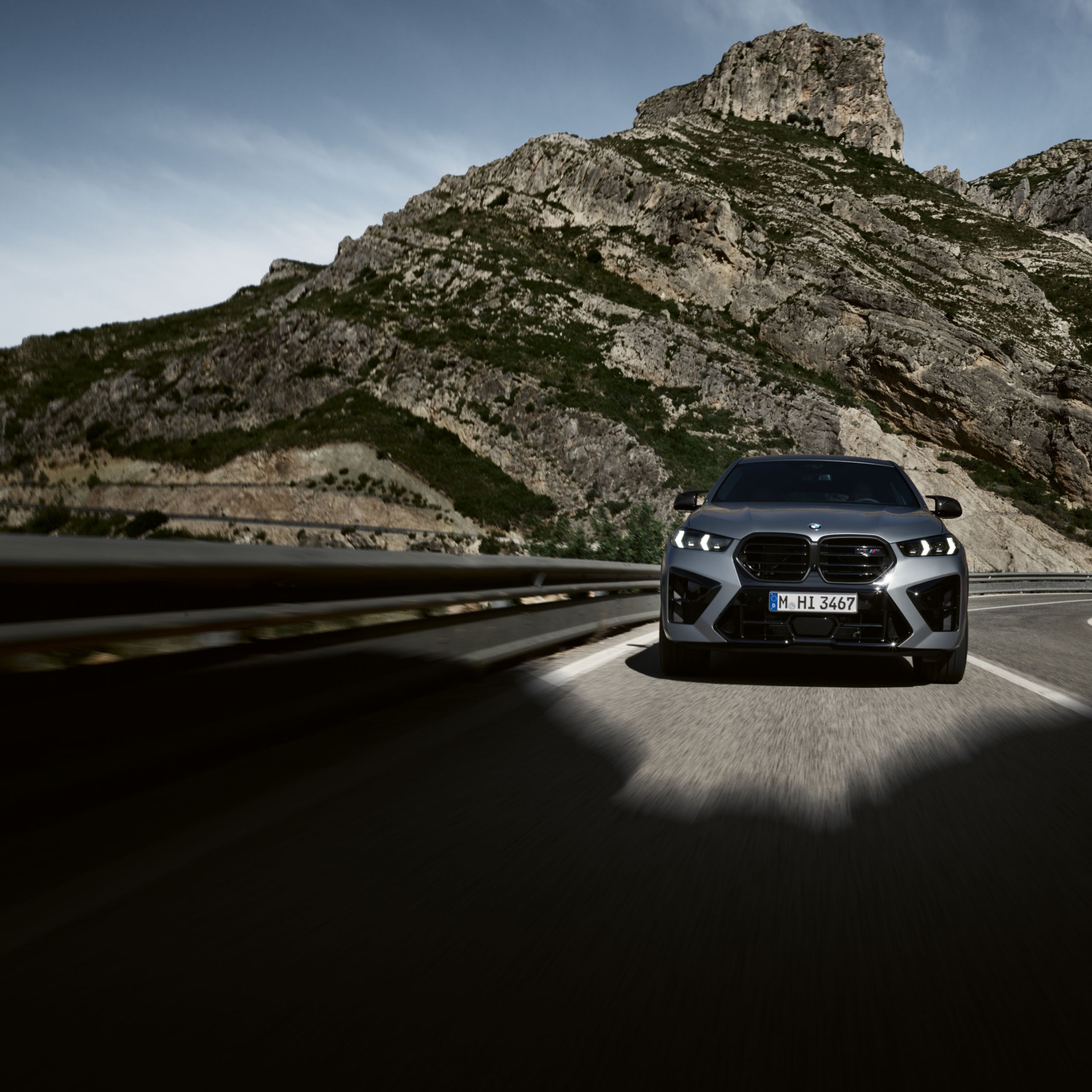 De BMW X6 M Competition rijdt door een vallei op een bochtige landweg