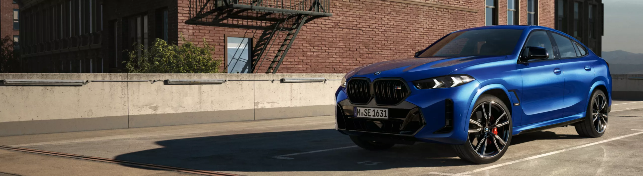 Ein BMW X6 SUV steht im Sonnenlicht auf einem Parkplatz vor einem Ziegelsteingebäude
