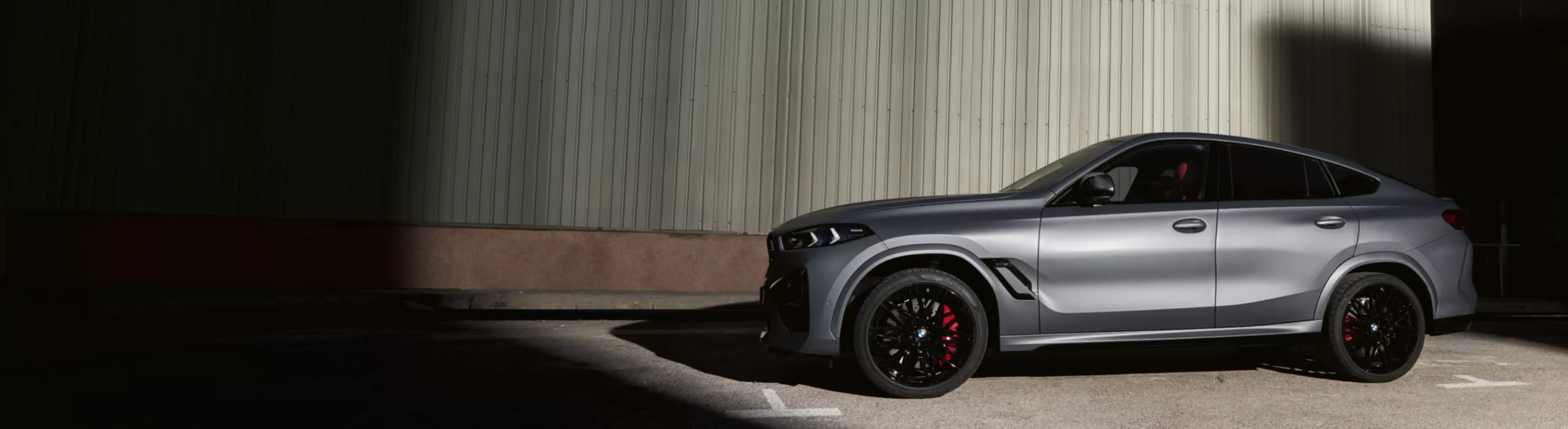 BMW X6 M Competition fährt auf einer kurvigen Landstraße durch ein Tal