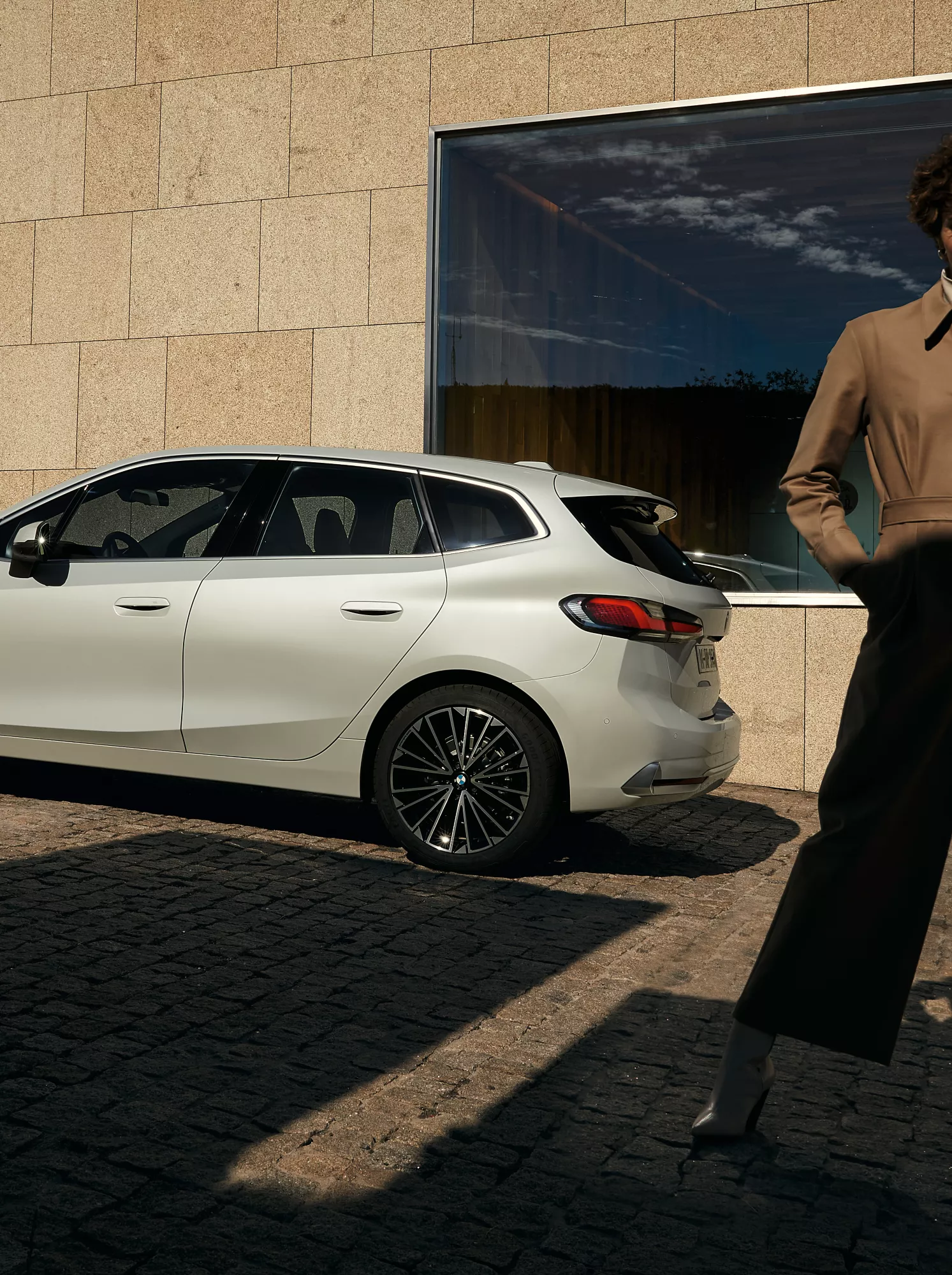 近代的なアパートの前に駐車しているBMW 2シリーズ アクティブ ツアラーとその横を歩いている人物 