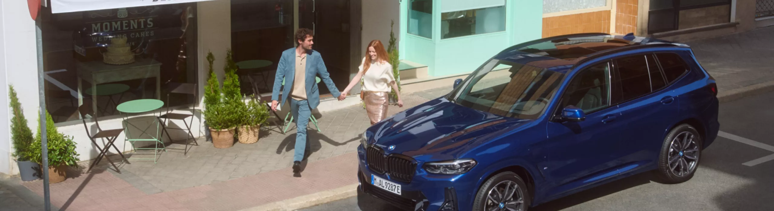 Zwei Personen gehen Hand in Hand auf dem Gehweg. Am Strassenrand ist ein BMW geparkt