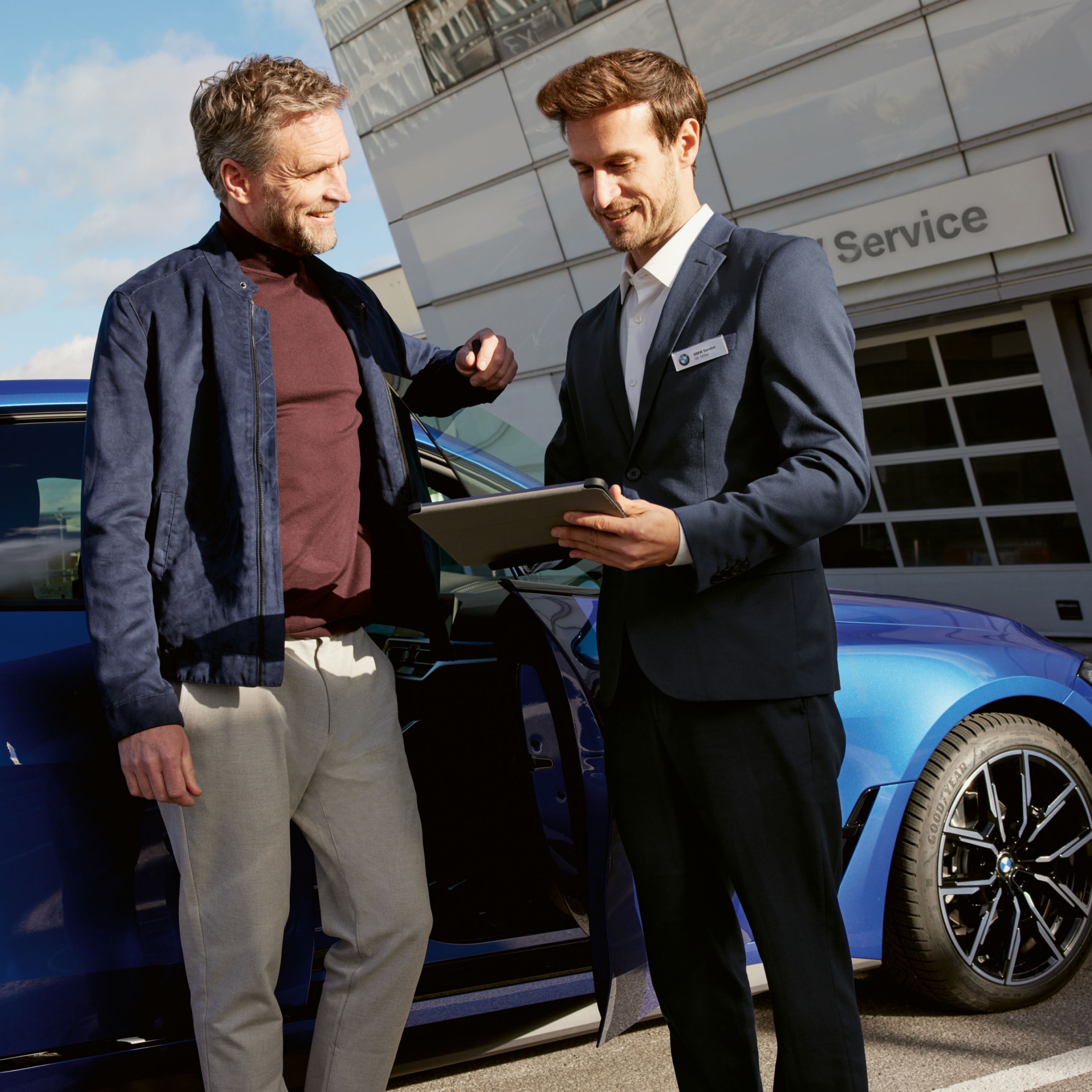 Zamestnanec stojí vedľa zákazníka s tabletom, pričom v pozadí je viditeľné BMW