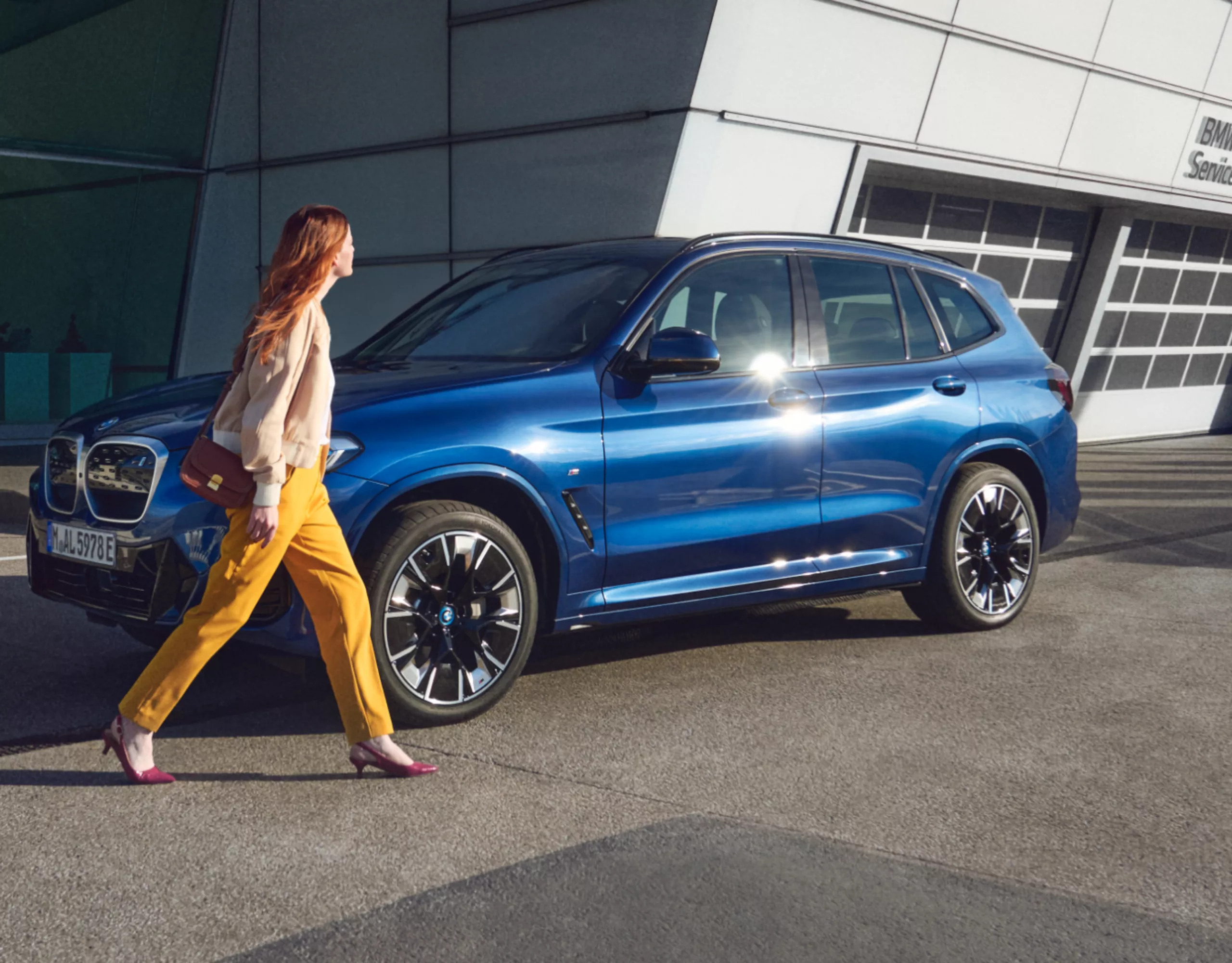 Une BMW se trouve devant un bâtiment. Une femme passe devant