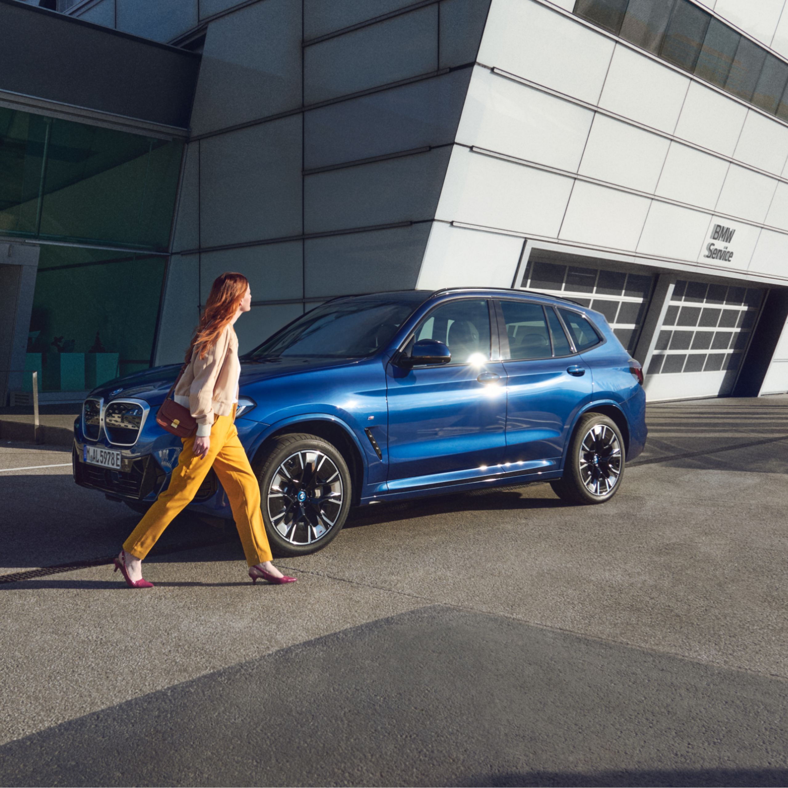 BMW stojí pred budovou. Žena beží okolo neho