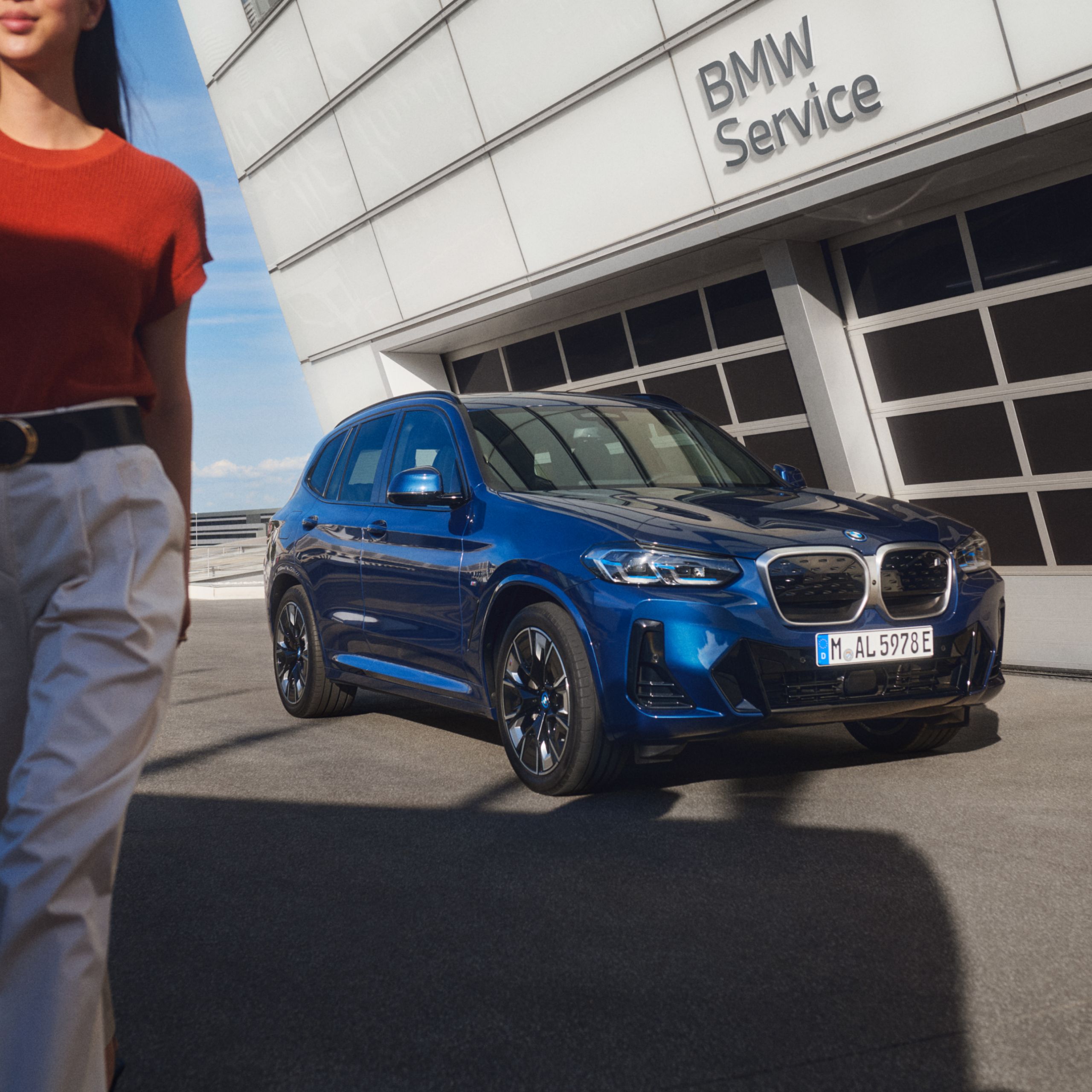 BMW stojí pred budovou. Človek čiastočne vybieha mimo záber