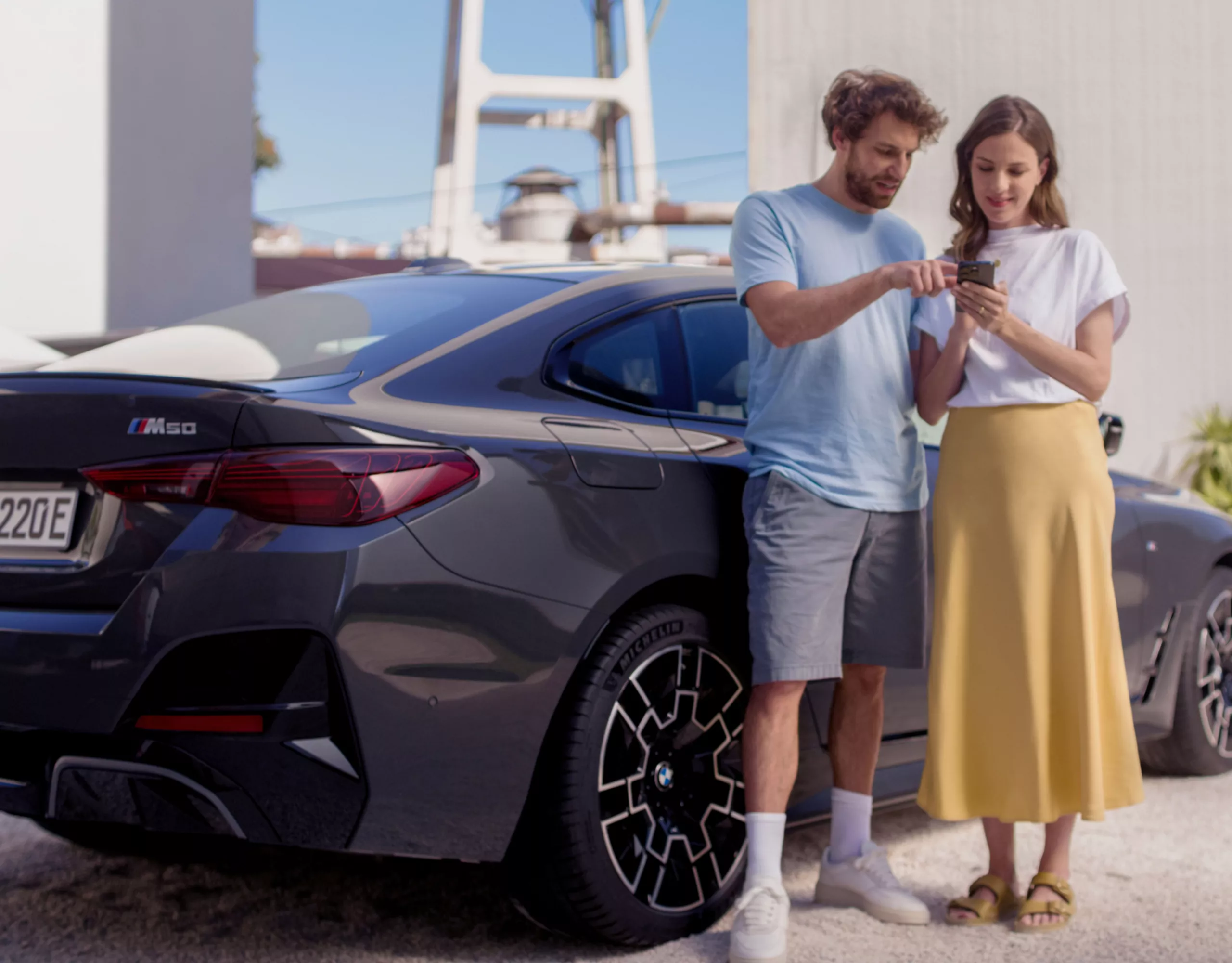 Vor einem BMW stehen ein Mann und eine Frau, die gemeinsam auf ein Smartphone schauen