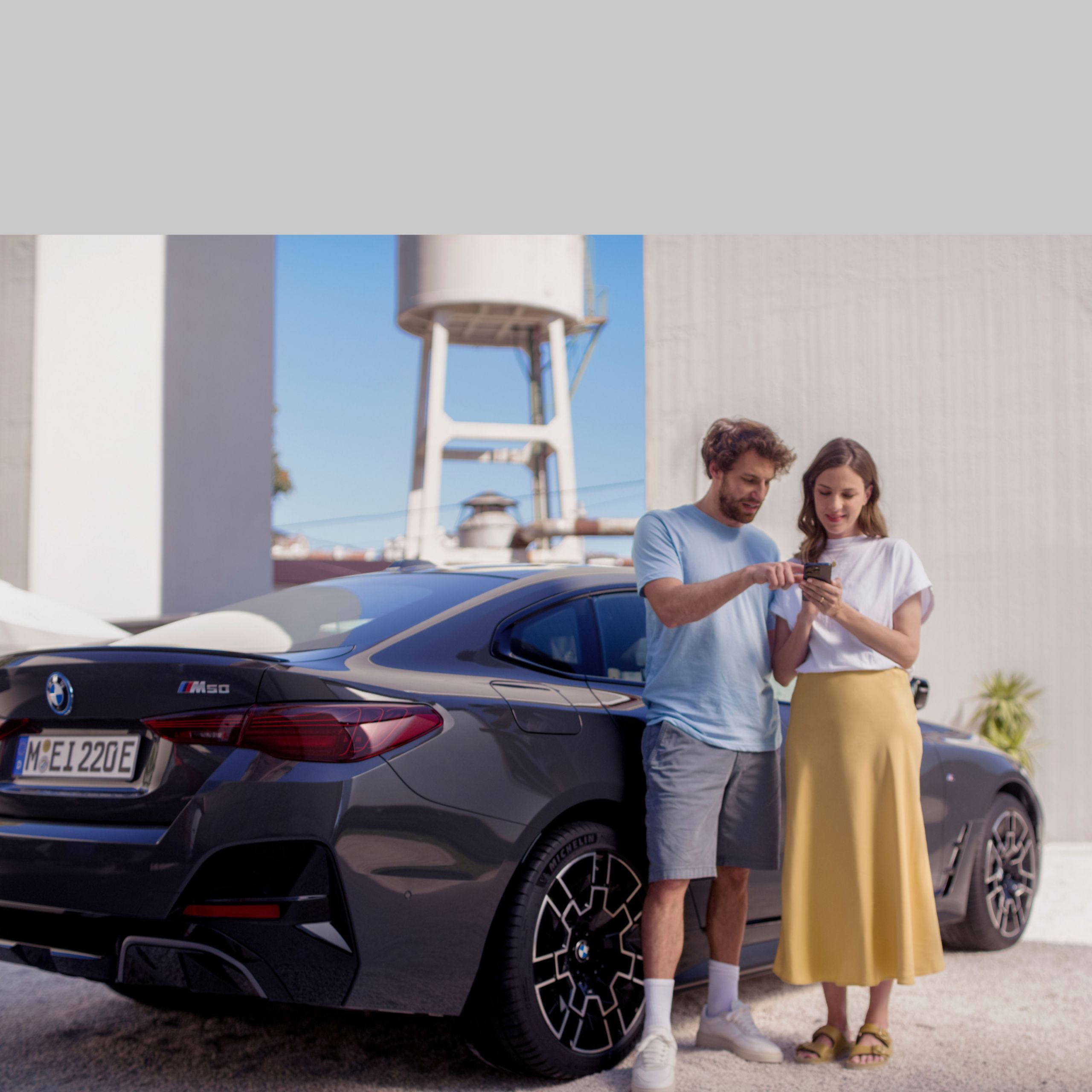 Muž a žena stoja pred BMW a spoločne a pozerajú sa na smartfón