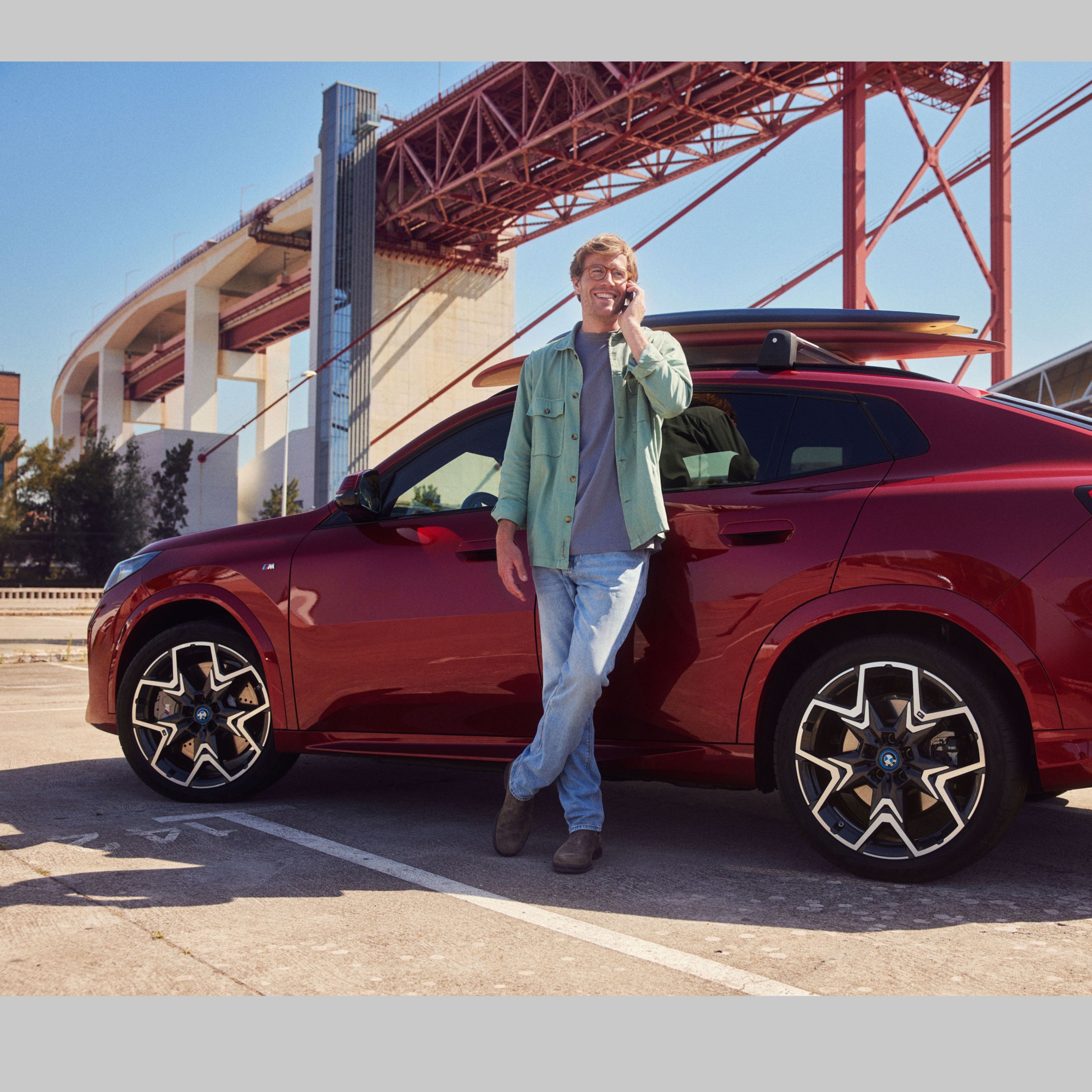 Muž sa opiera o svoje BMW a telefonuje. V pozadí vidieť most