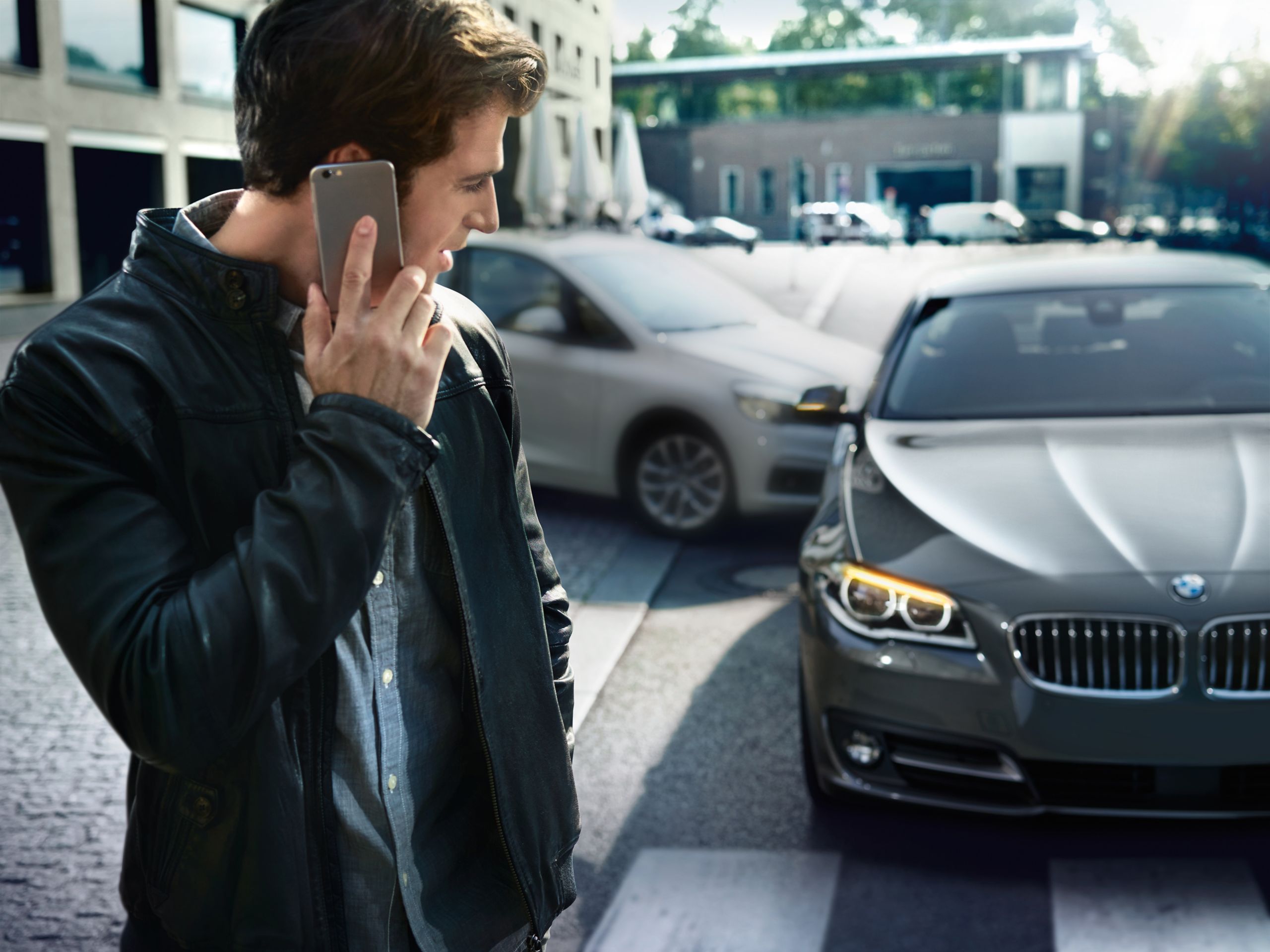 A man on his cell phone looking at a BMW that has been in a small collision.