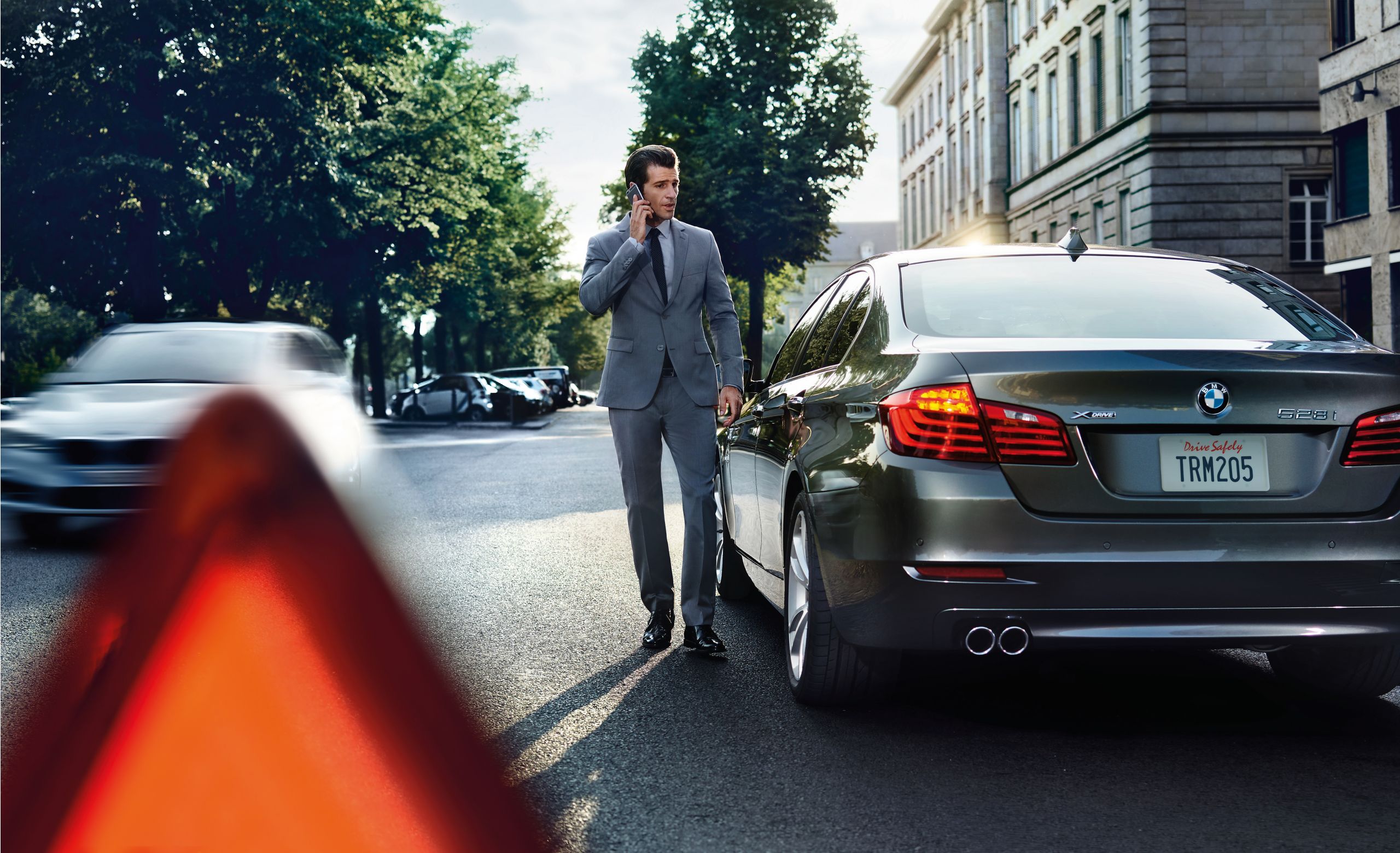 A businessman on a cell phone standing next to a BMW.