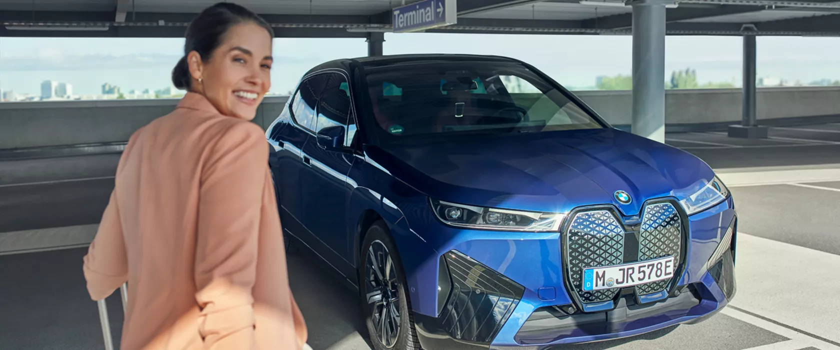 Eine Frau steht lächelnd vor ihrem blauem BMW.