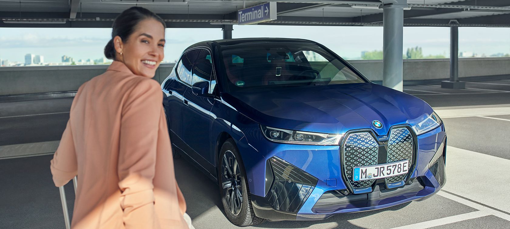 Eine lachende Frau nähert sich einem stehenden BMW.